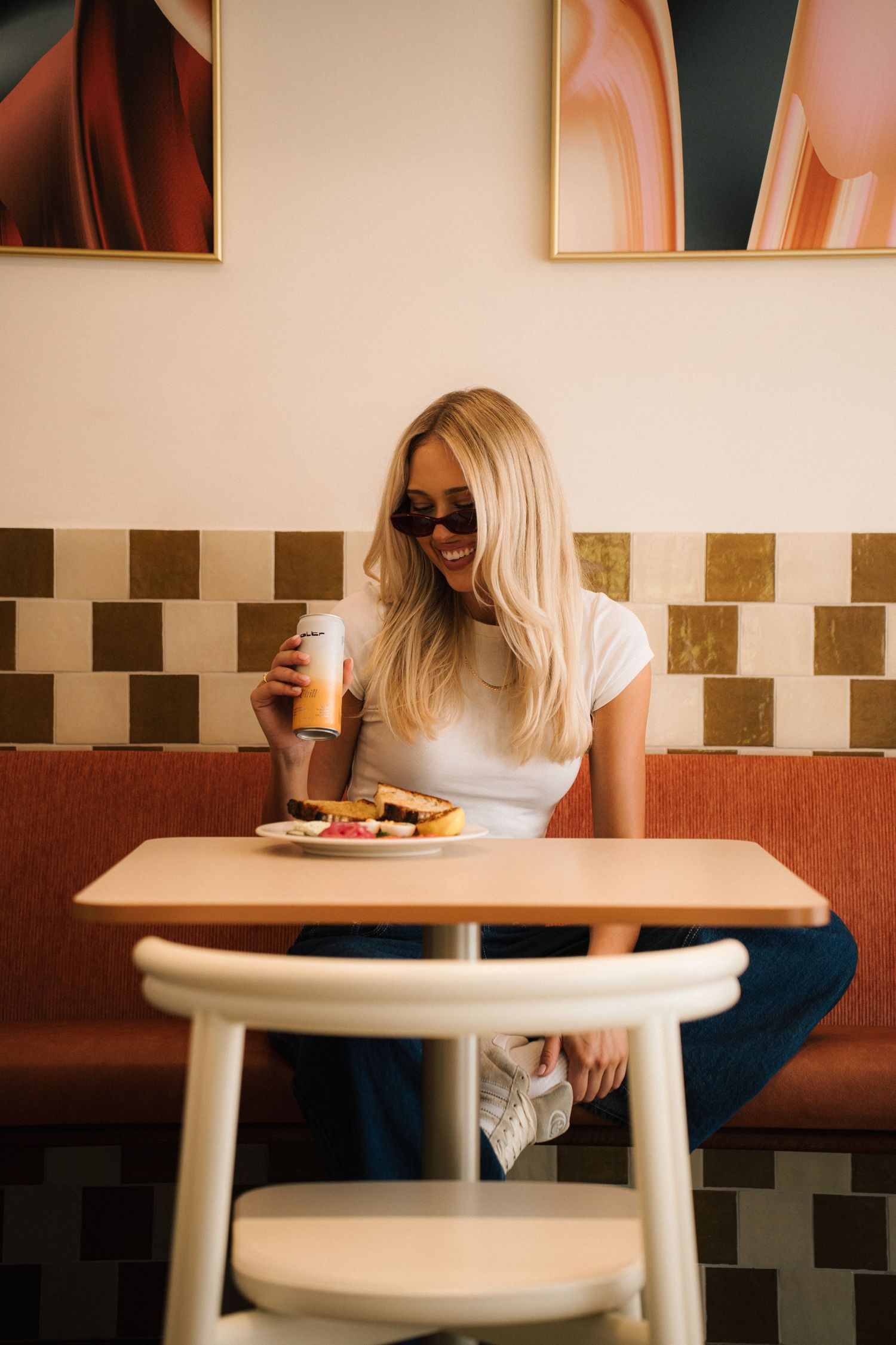 Person in sunglasses enjoying coffee and food at a retro diner with checkerboard wall tiles and abstract art decor.