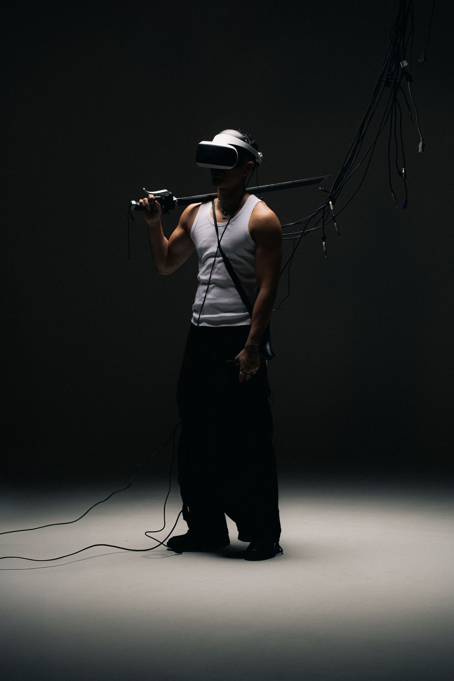 Dramatic silhouette of a photographer wearing a hat and tank top holding a light stand against dark background.