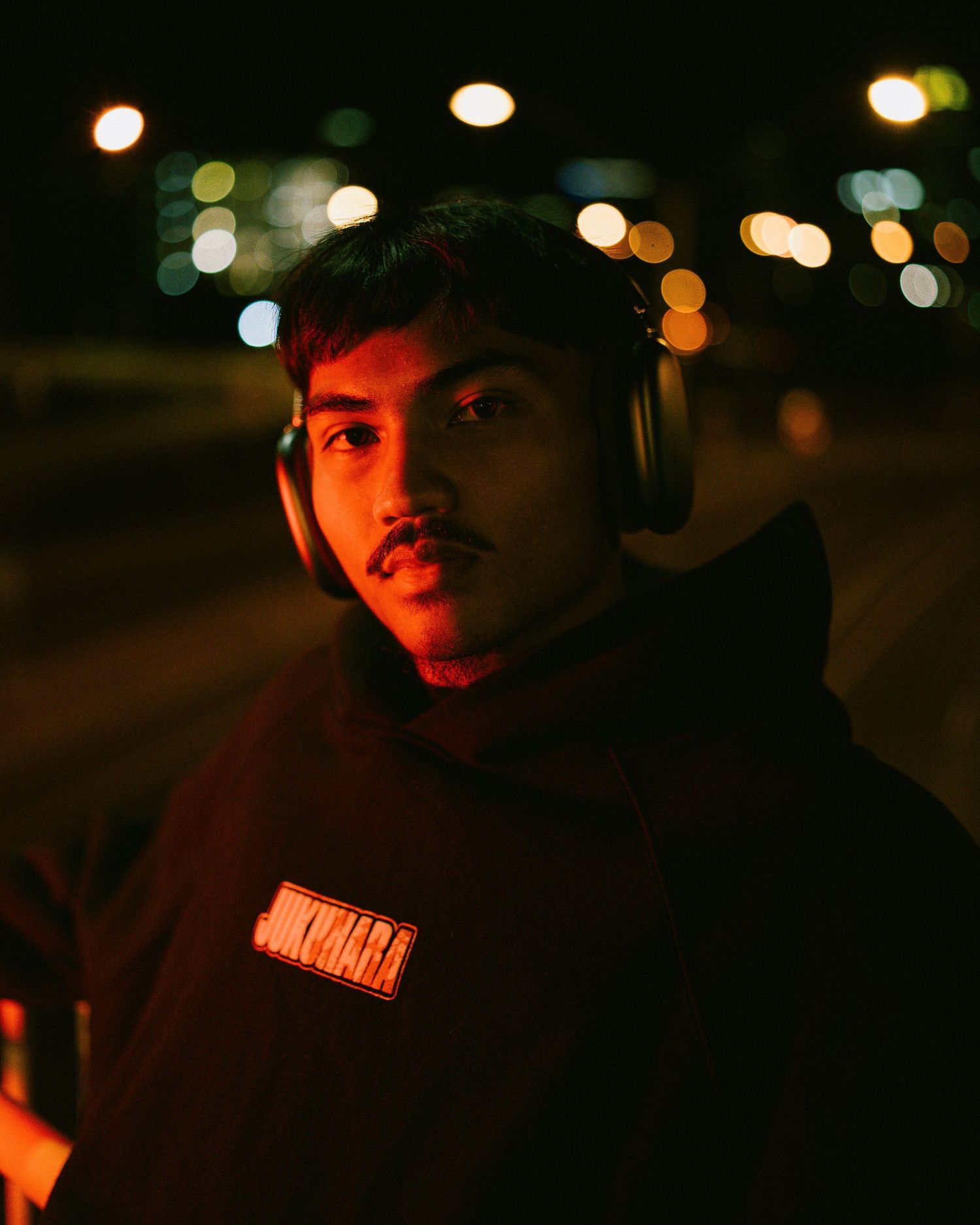 Person wearing headphones and hoodie illuminated by red light at night.