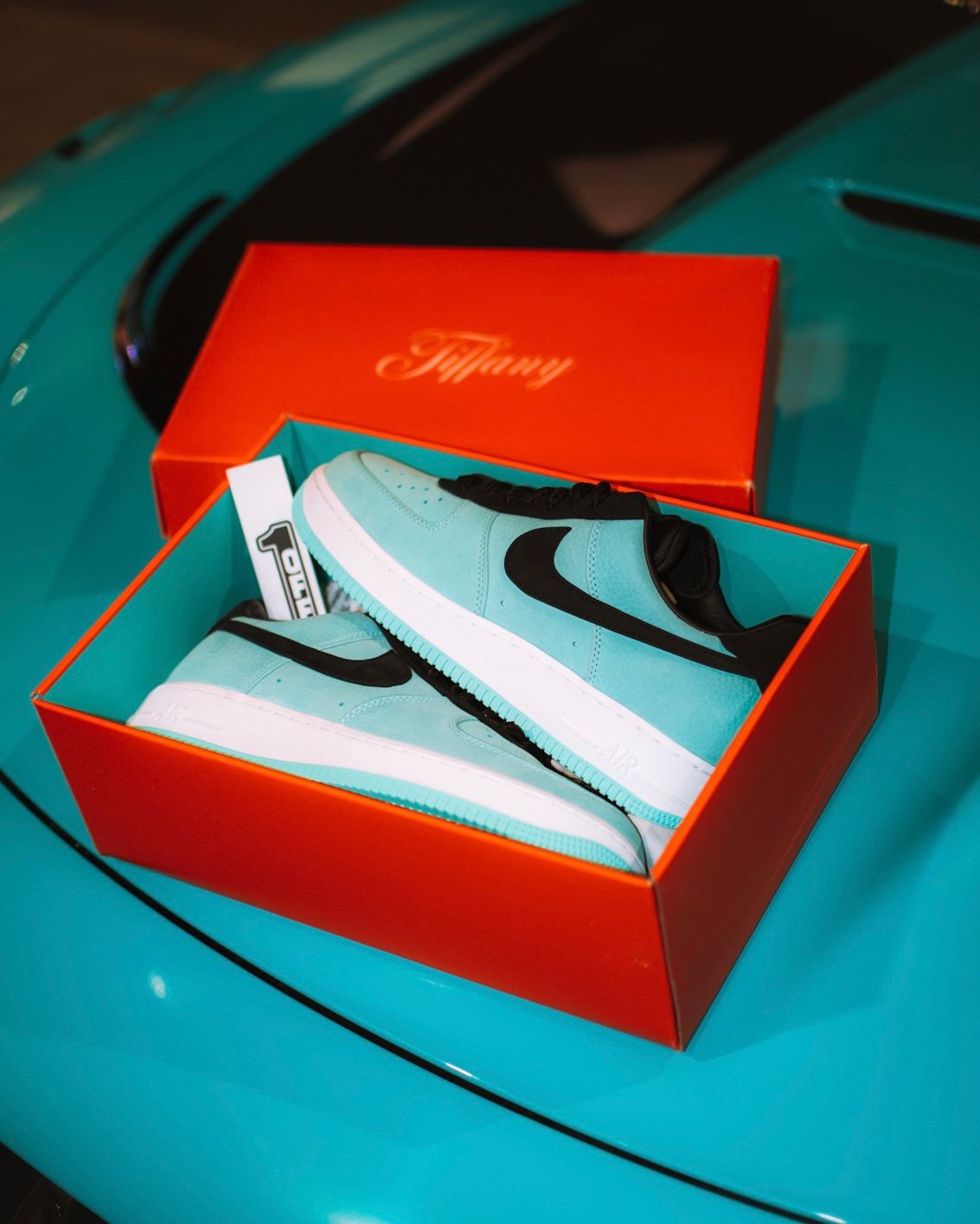 Nike sneakers in mint green and black colorway displayed in a red Tiffany box on turquoise surface.