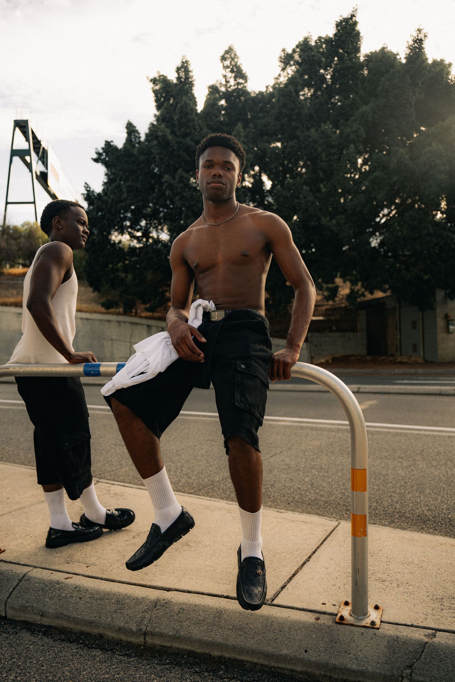 Casual streetwear scene with two people standing by a metal pole on a sunny day.