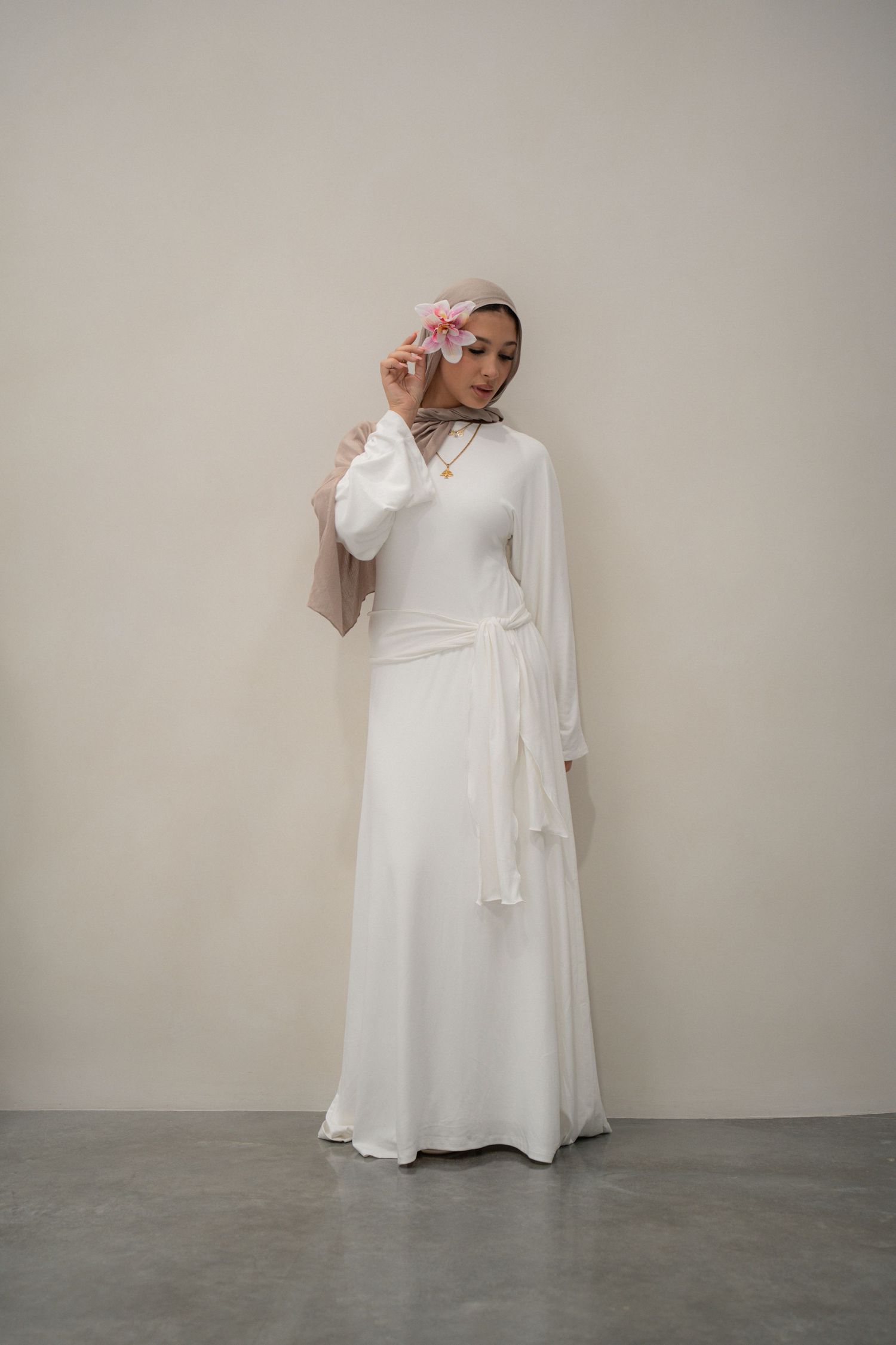 Elegant white wrap dress with long sleeves styled with floral headpiece in studio setting.