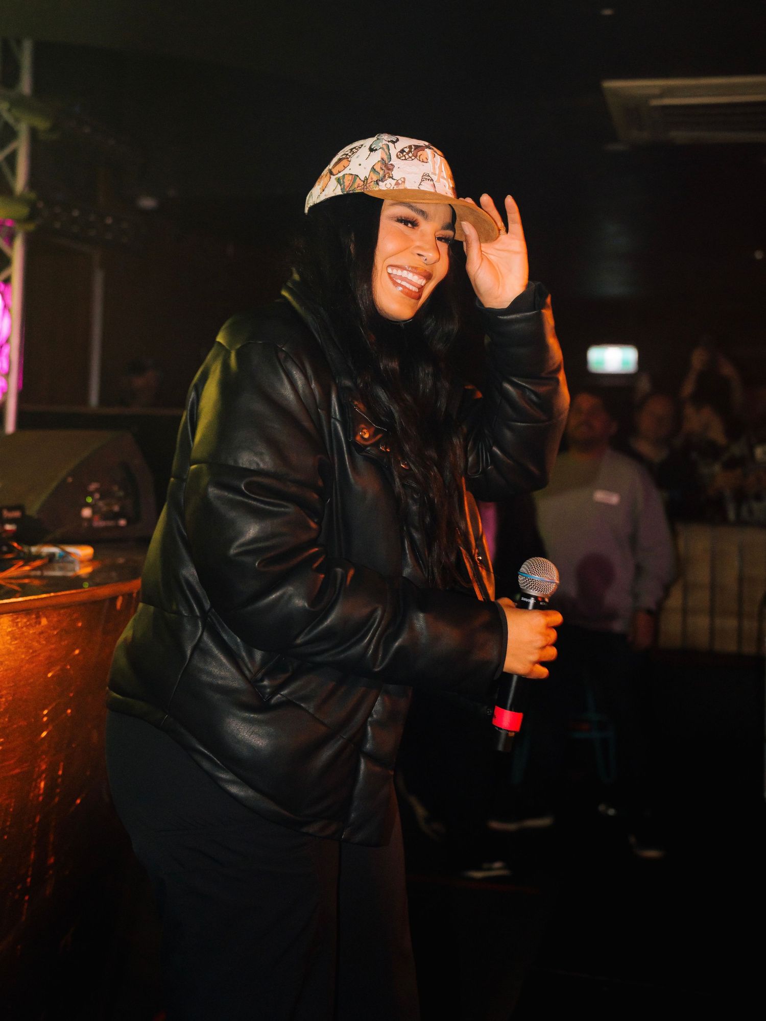 Person in a black puffer jacket dancing at a dimly lit nightclub with colorful lighting effects in the background.