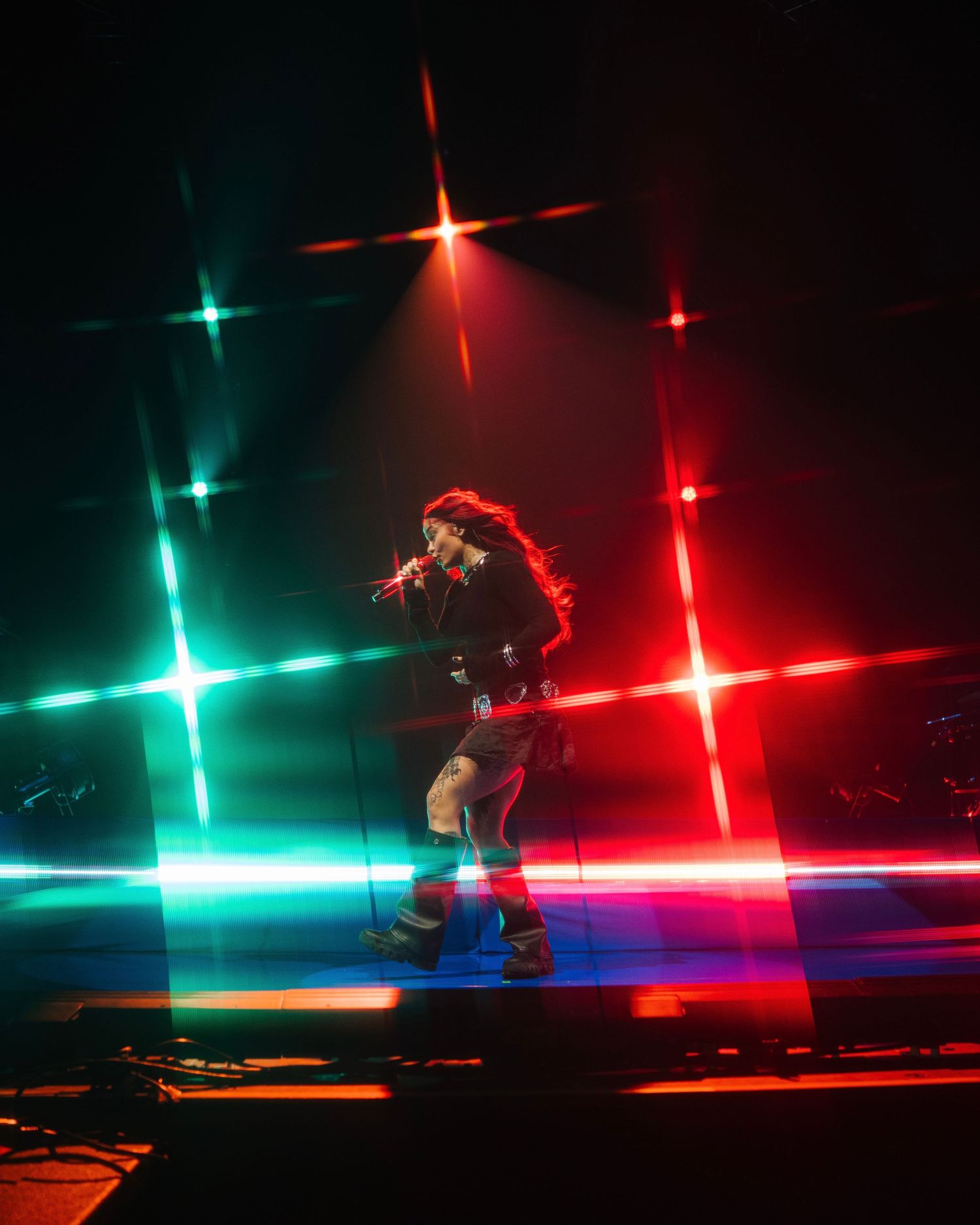 Performer silhouetted against dramatic red and green light beams on stage.