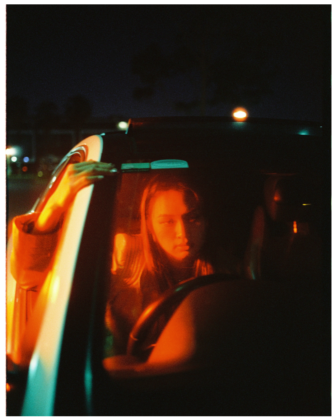 A figure illuminated in warm orange light sits in a car at night with a glowing atmosphere around them.