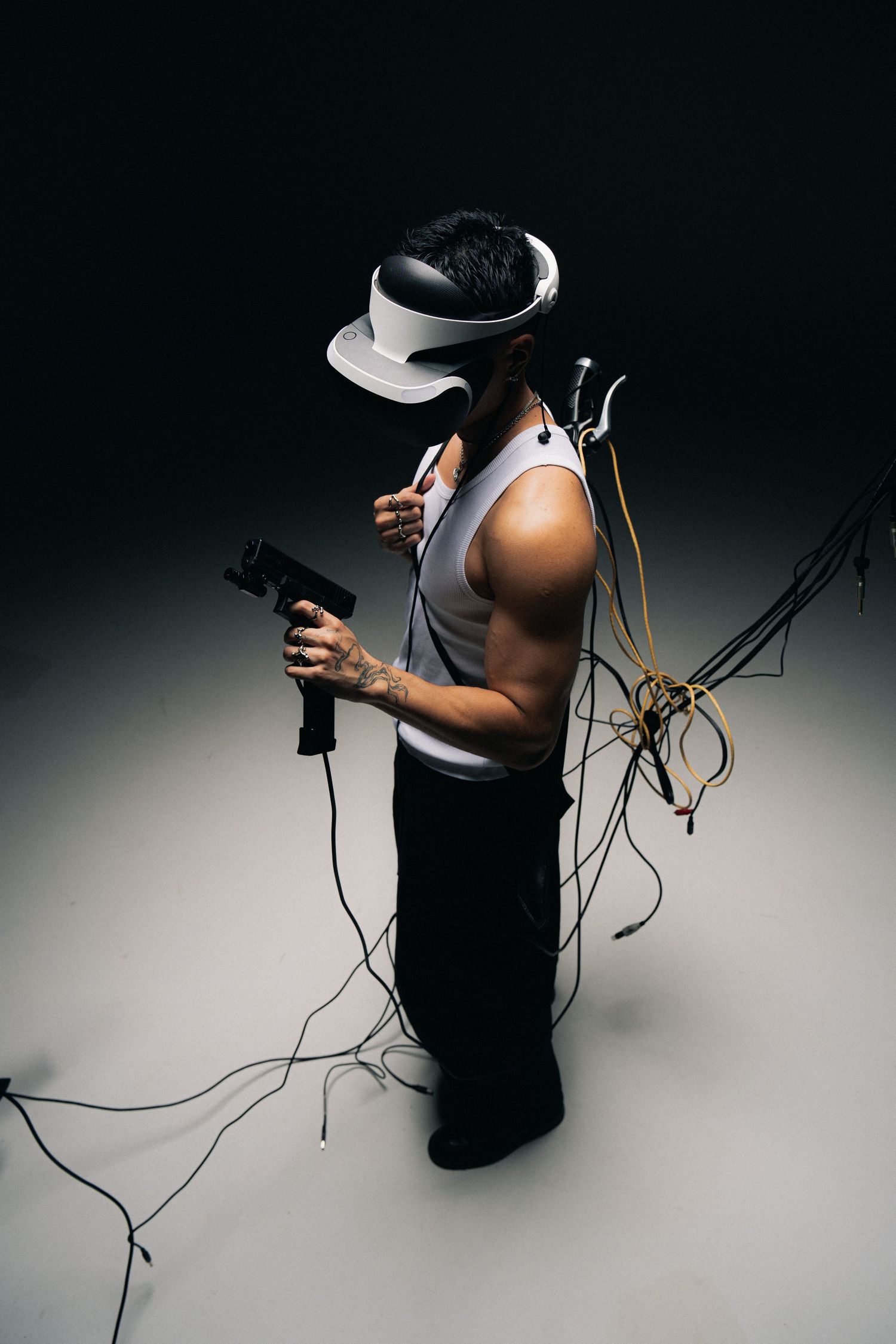 Person wearing VR headset standing with wired cables and holding game controller in dark studio setting.