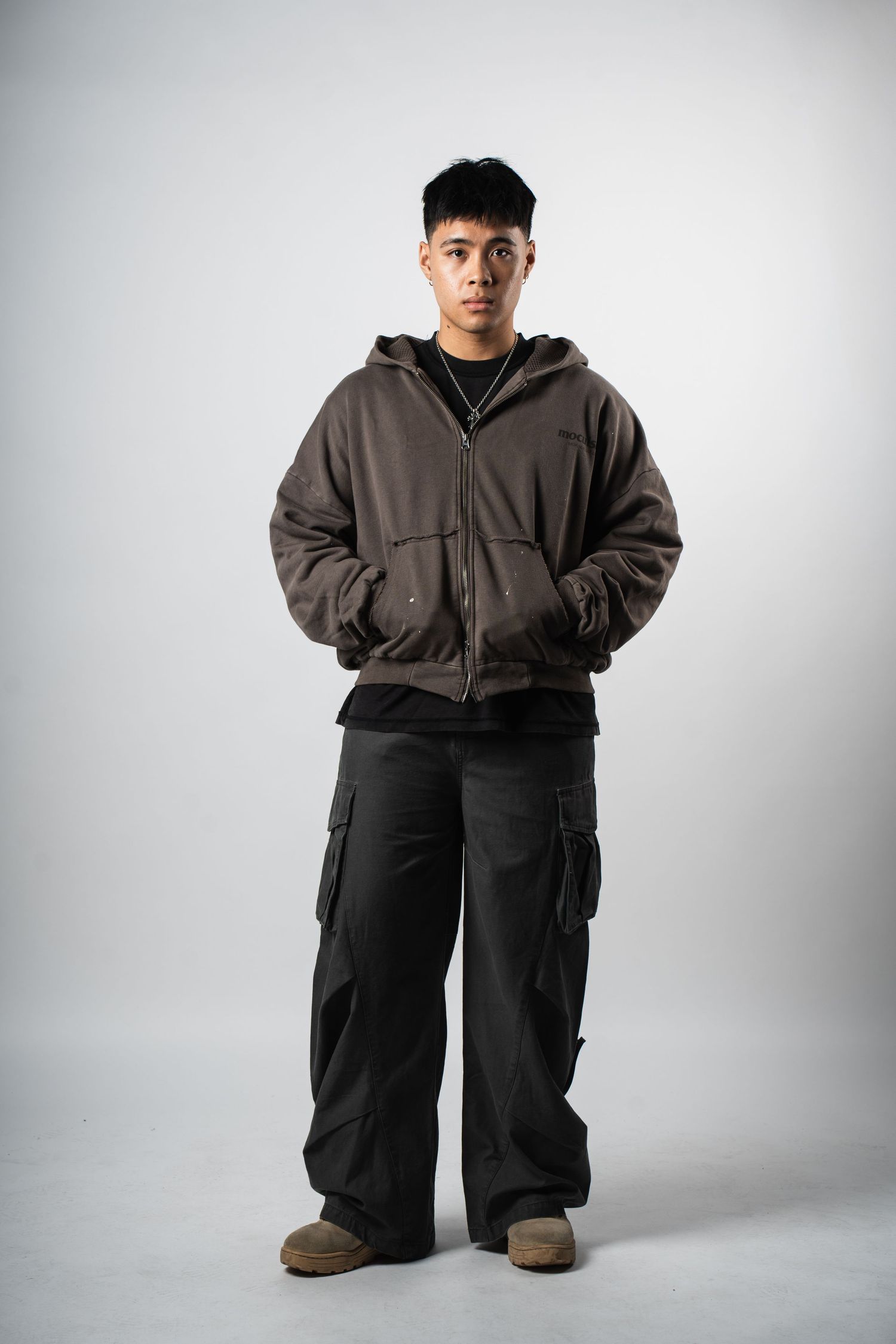 Person in brown bomber jacket and cargo pants posing against white background.