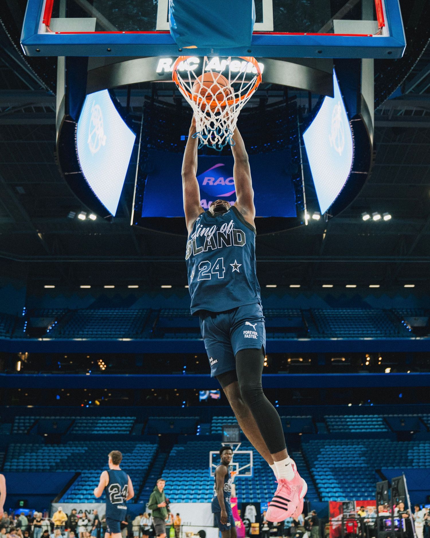 Basketball player in blue jersey performs a slam dunk in an indoor arena.