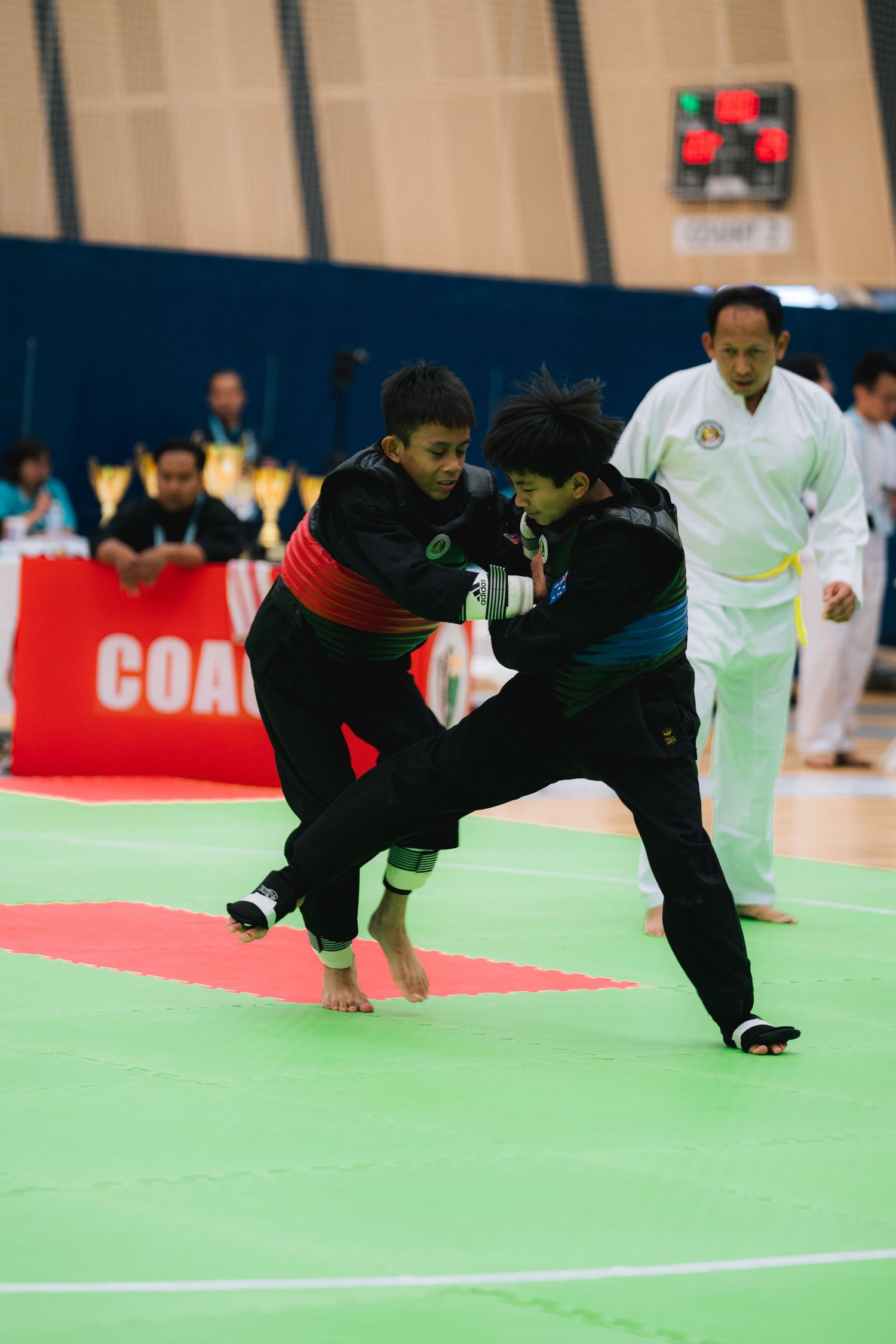 Martial artists in black uniforms spar on a green mat during a competition.