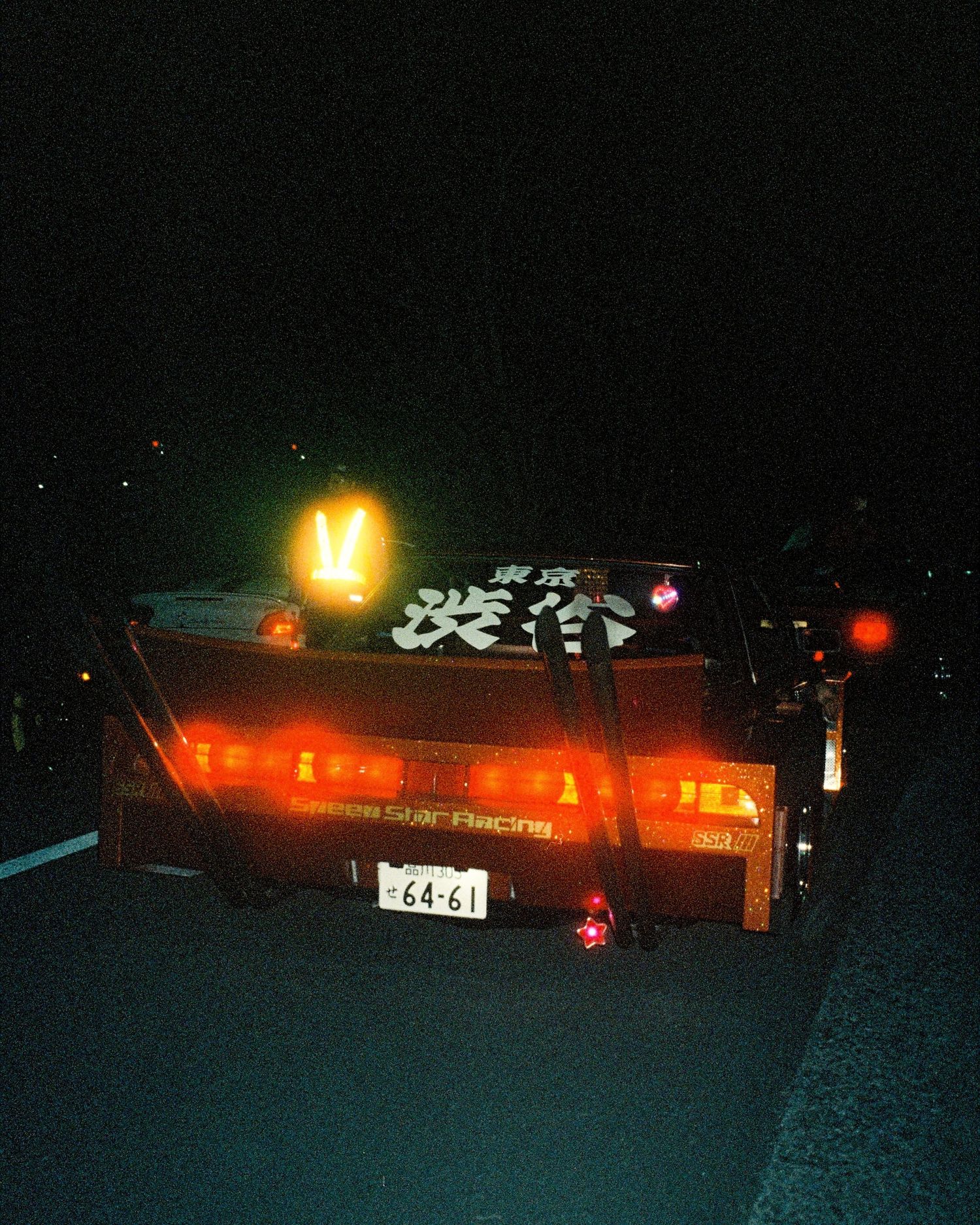 Illuminated taillights of modified Japanese car at night gathering.