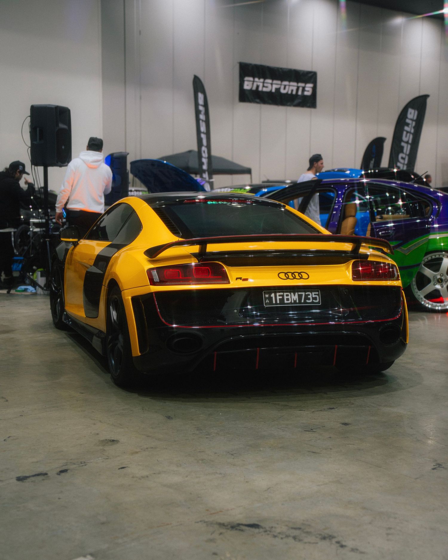 Yellow Audi R8 with black accents showcased at indoor automotive event.