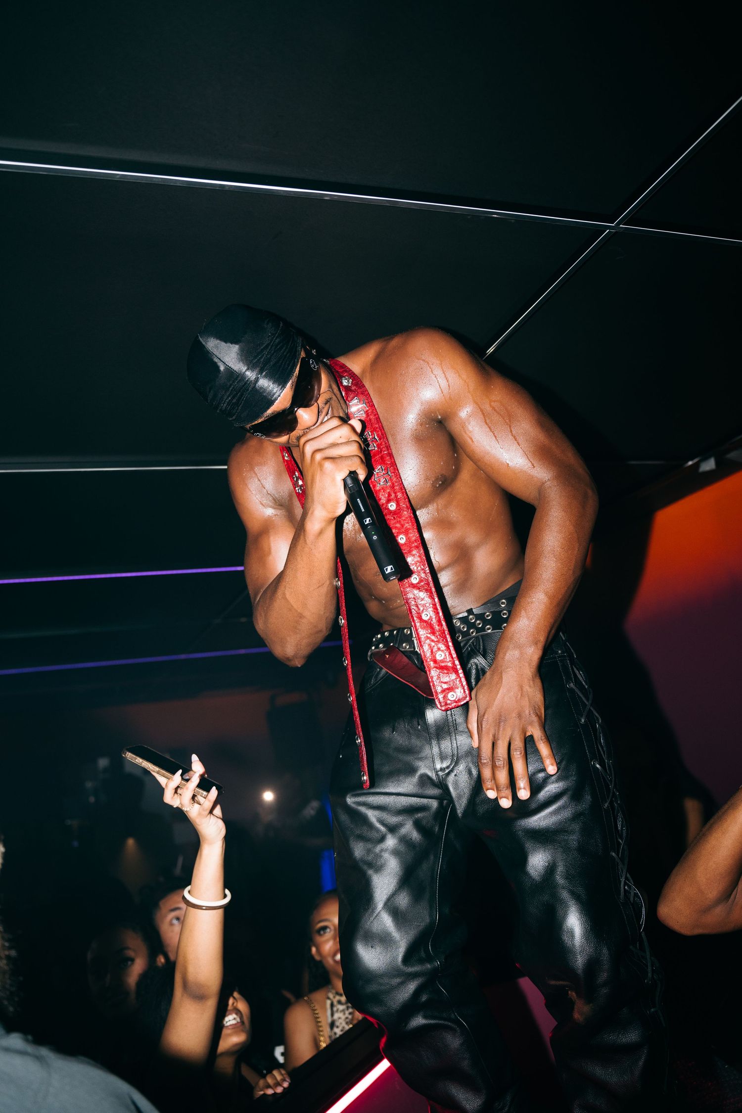 A performer on stage leans into the crowd during an energetic nightclub performance with dramatic lighting.