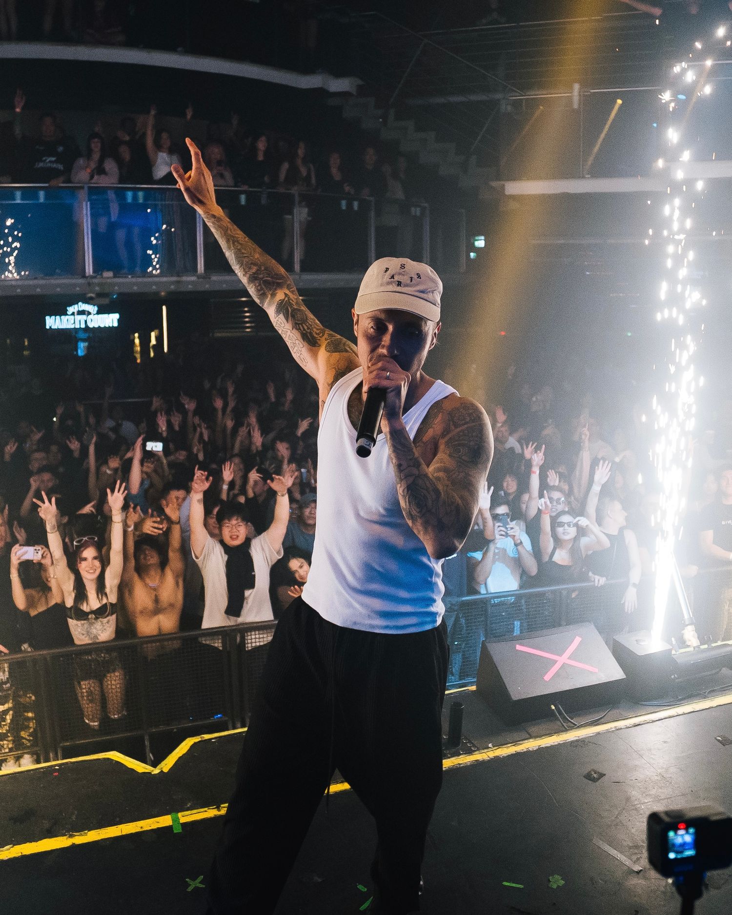 Energetic crowd with raised hands at a nightclub event as sparklers and stage lights create a lively atmosphere.