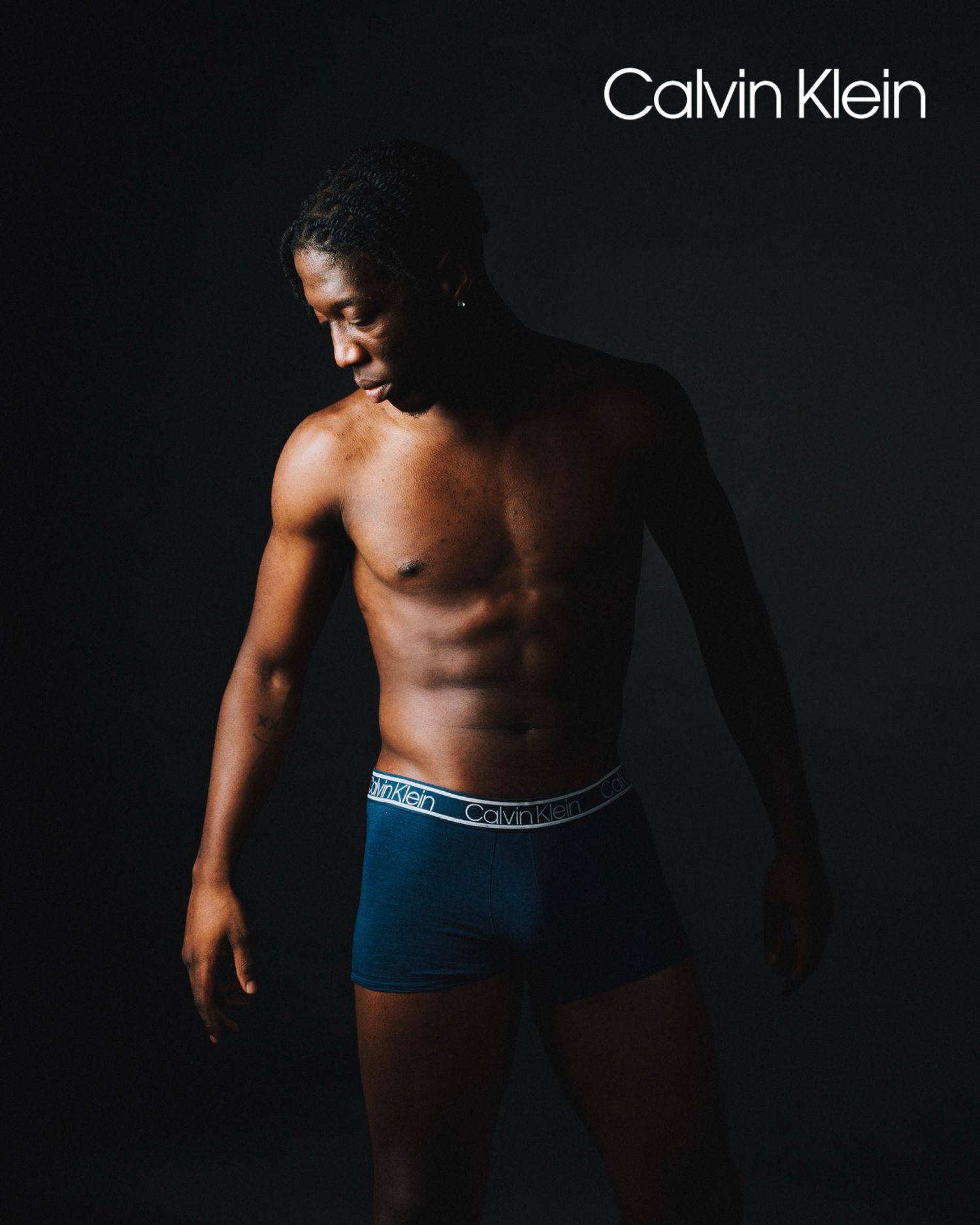 Calvin Klein underwear advertisement showing model in blue boxer briefs against dark background.