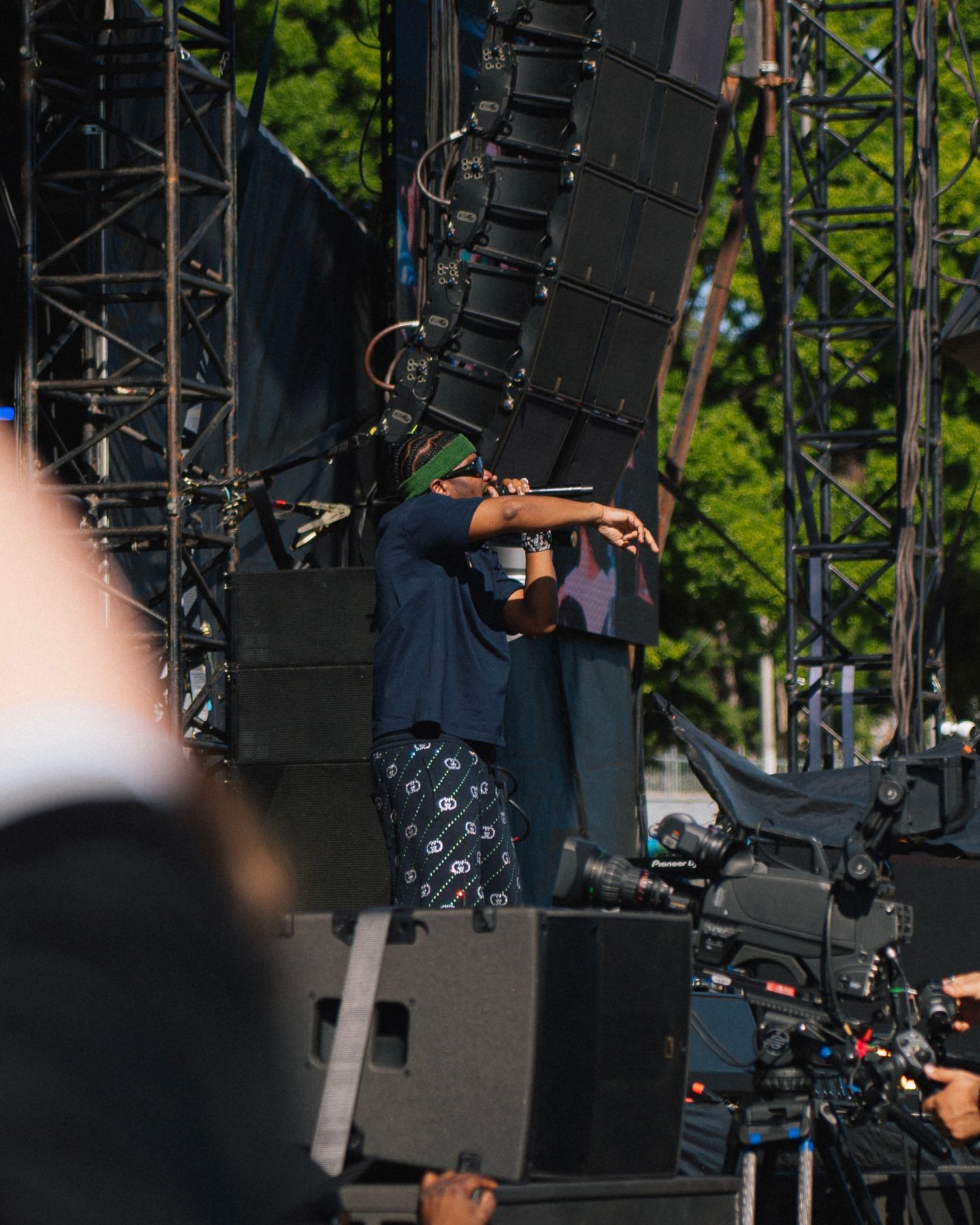 Performer on stage during an outdoor concert with large speaker arrays and sound equipment visible in the background.
