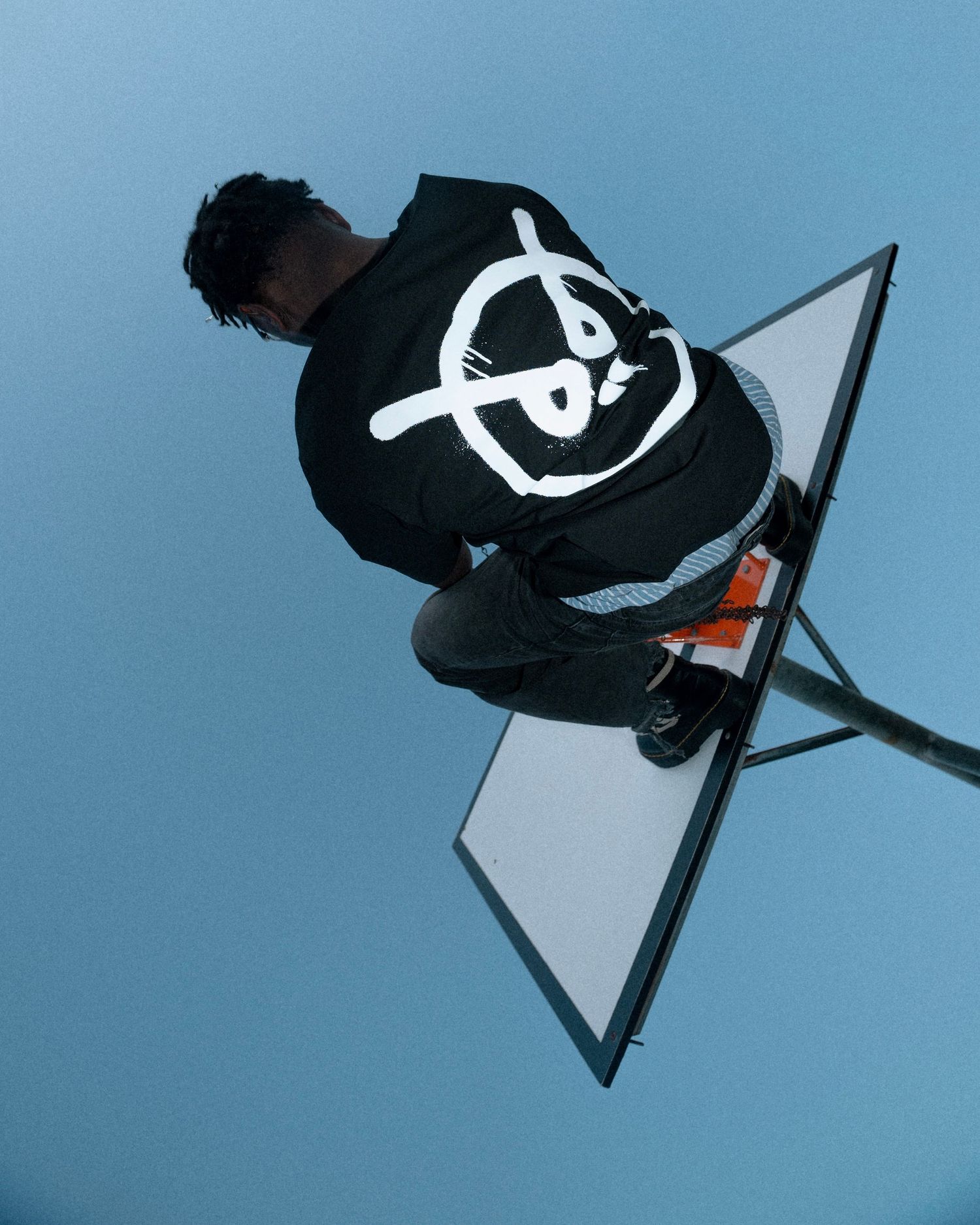 Person wearing a black hoodie with graphic design photographed from below against a blue sky.