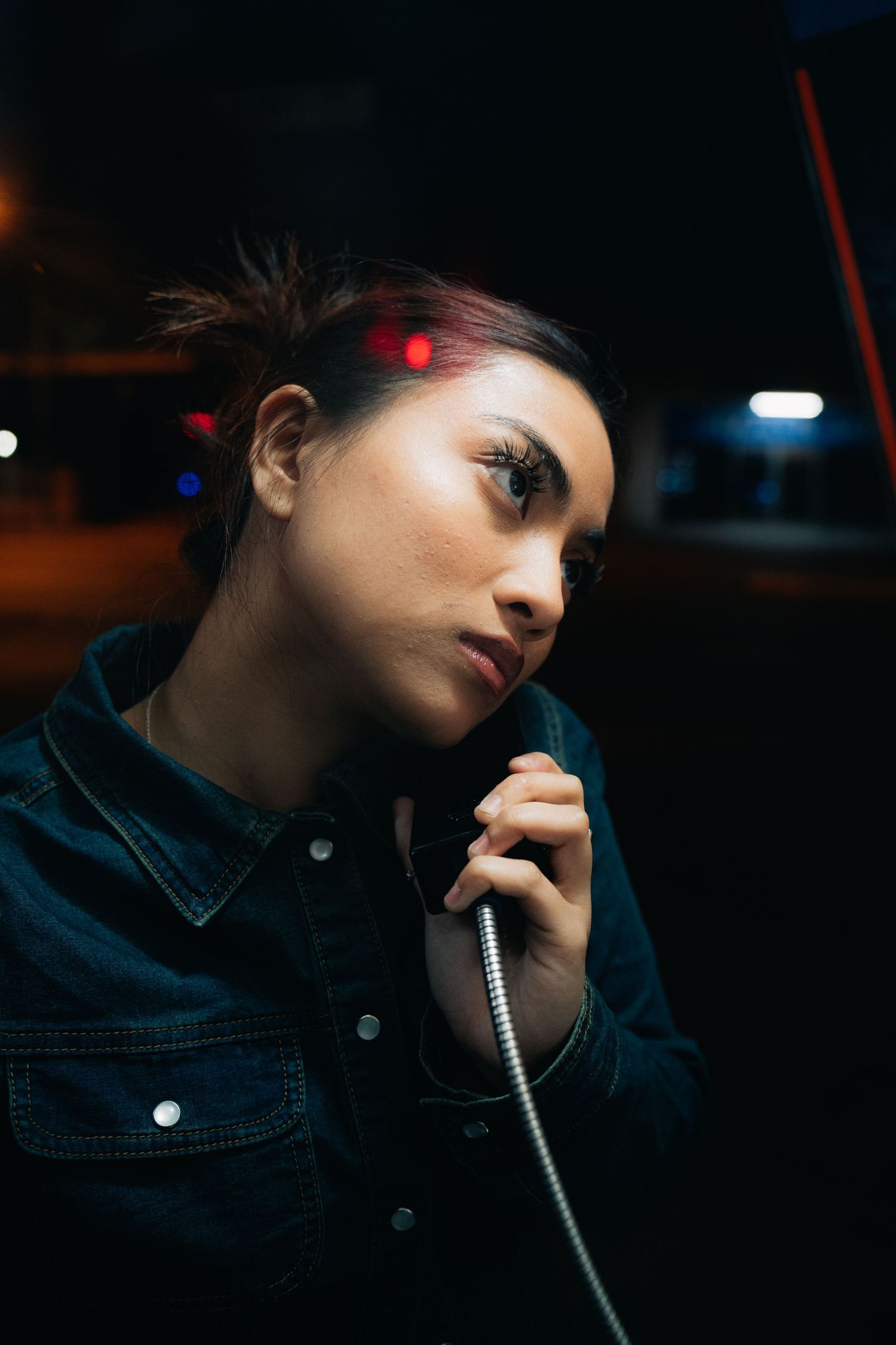 A moody nighttime portrait of someone holding a telephone cord while wearing a denim jacket.