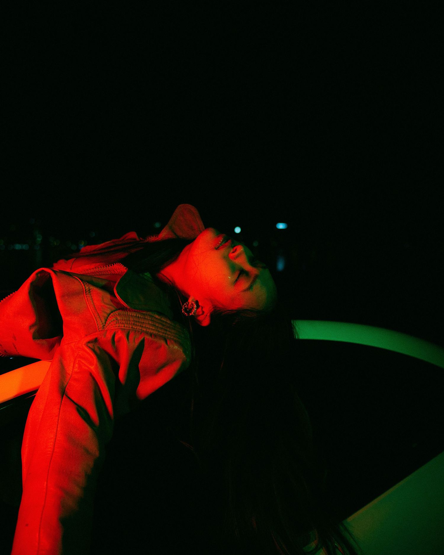 Artistic portrait illuminated by dramatic red and green lighting creating a moody nighttime atmosphere.