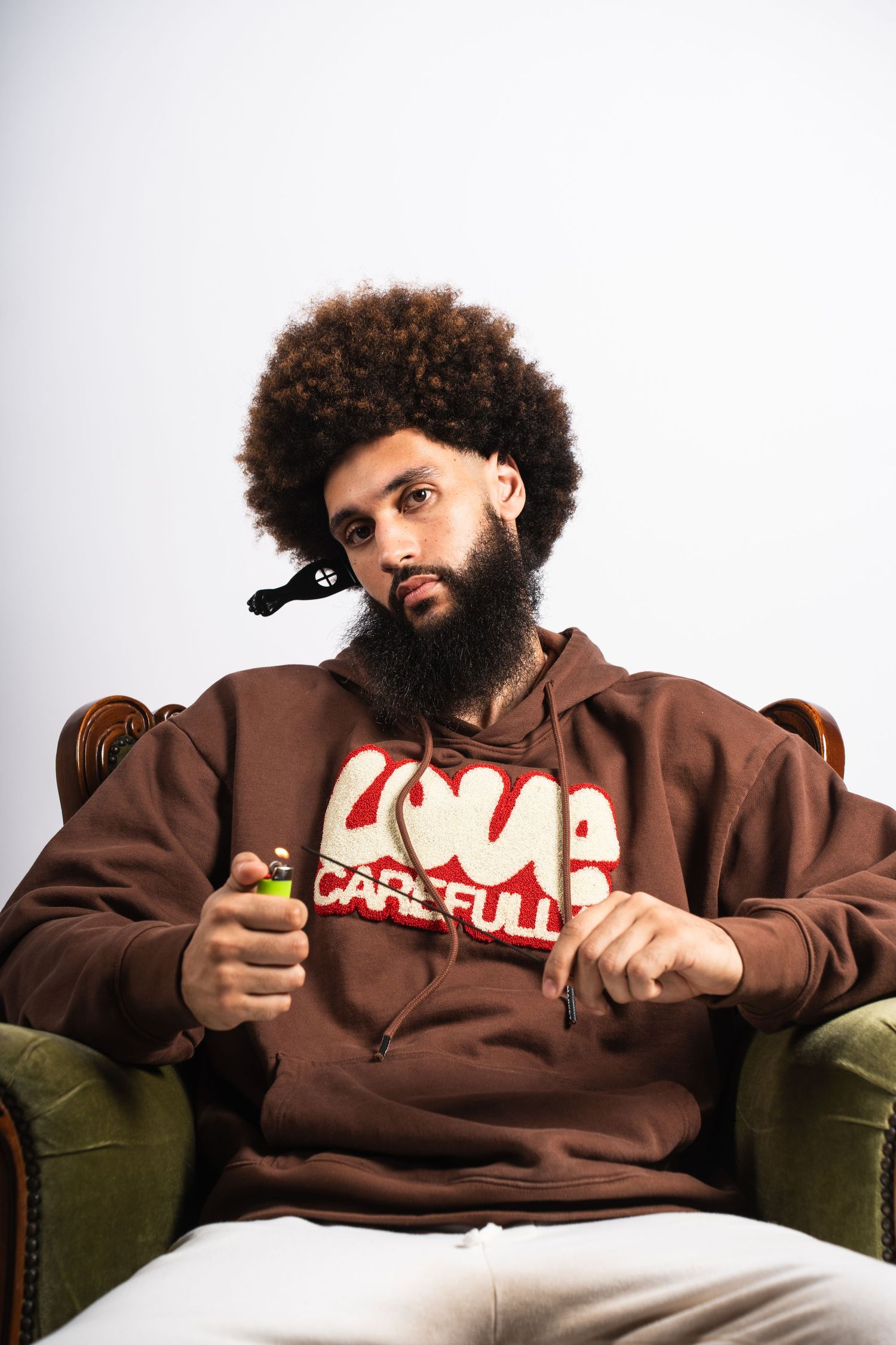 A person in a brown hoodie reclines comfortably on a vintage green couch in a white room in multiple poses.