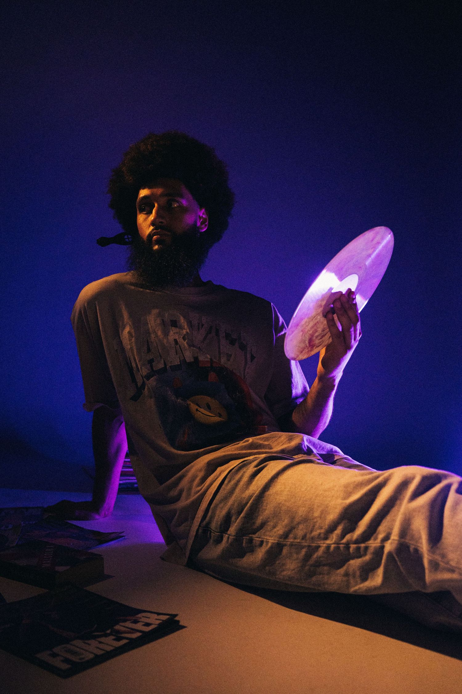 Person in casual attire sits against dark backdrop with purple lighting while holding illuminated object.
