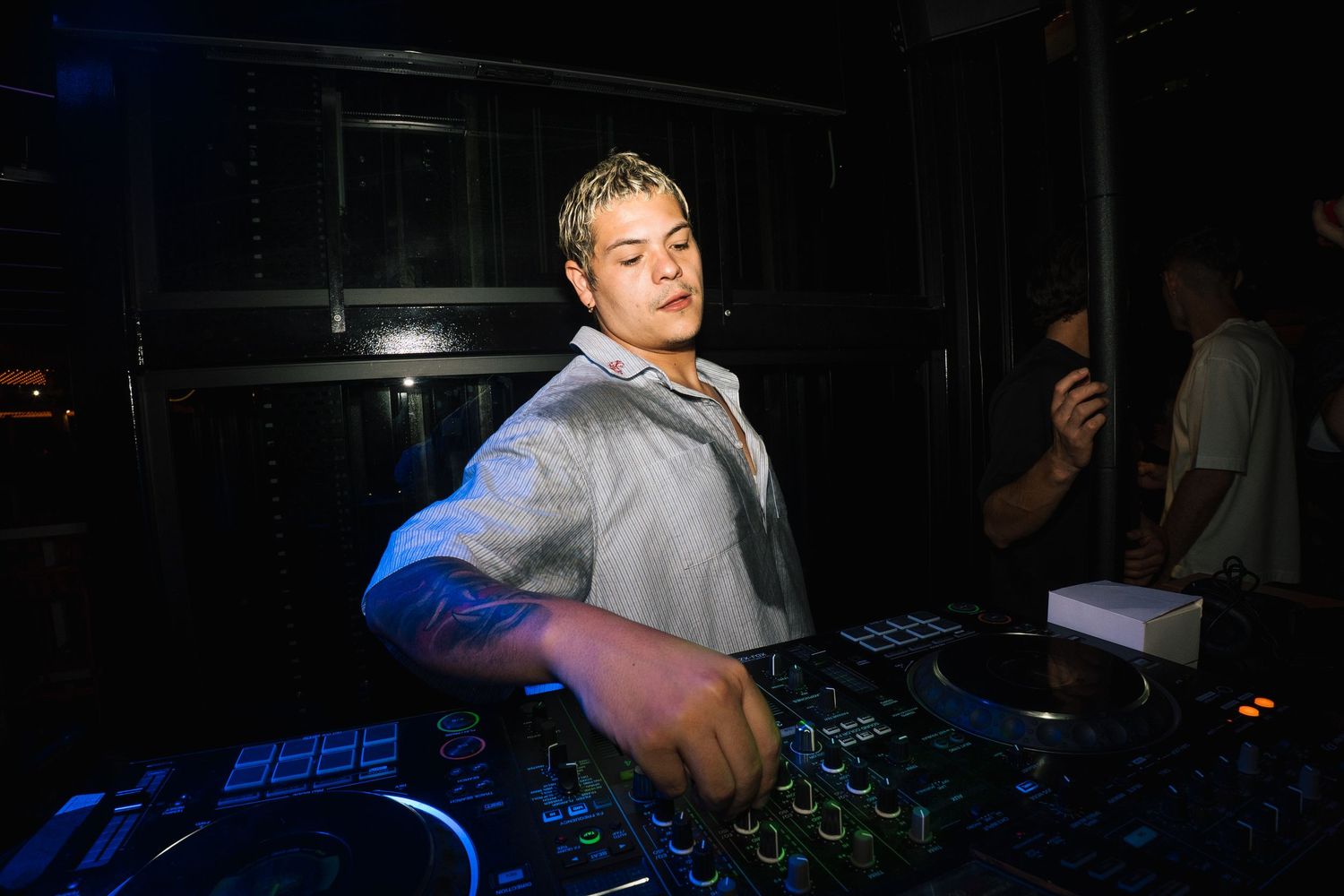 A DJ performs at a nightclub mixing desk illuminated by blue lighting in a dark environment.