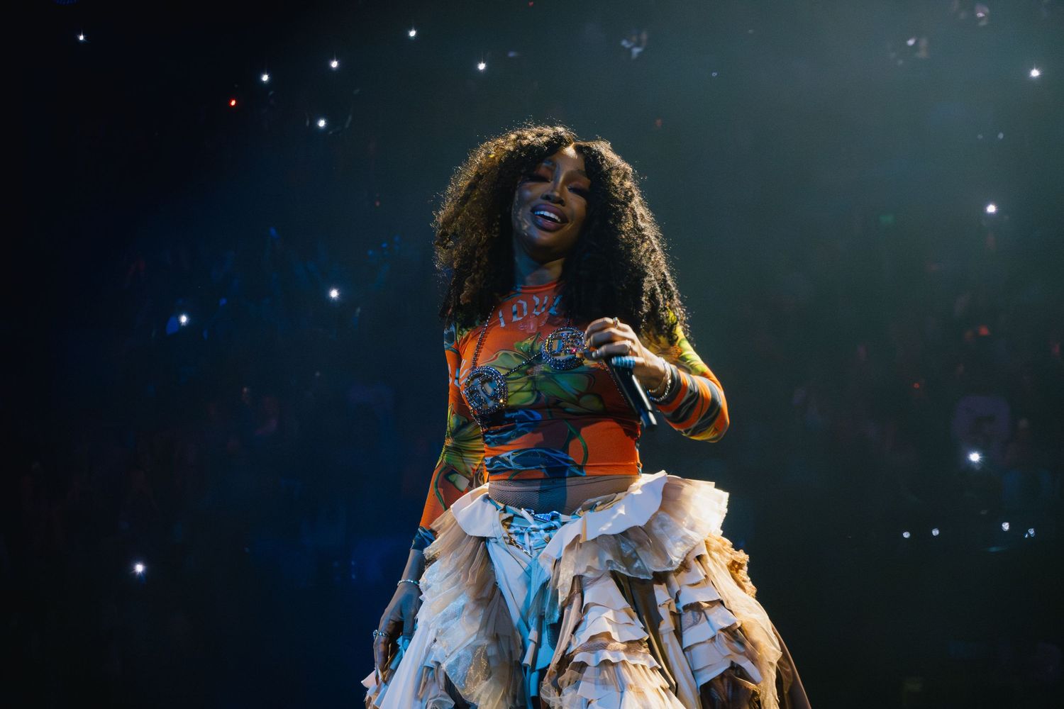 A performer in a flowing white dress stands on stage against a dark, starry background and theatrical lighting.