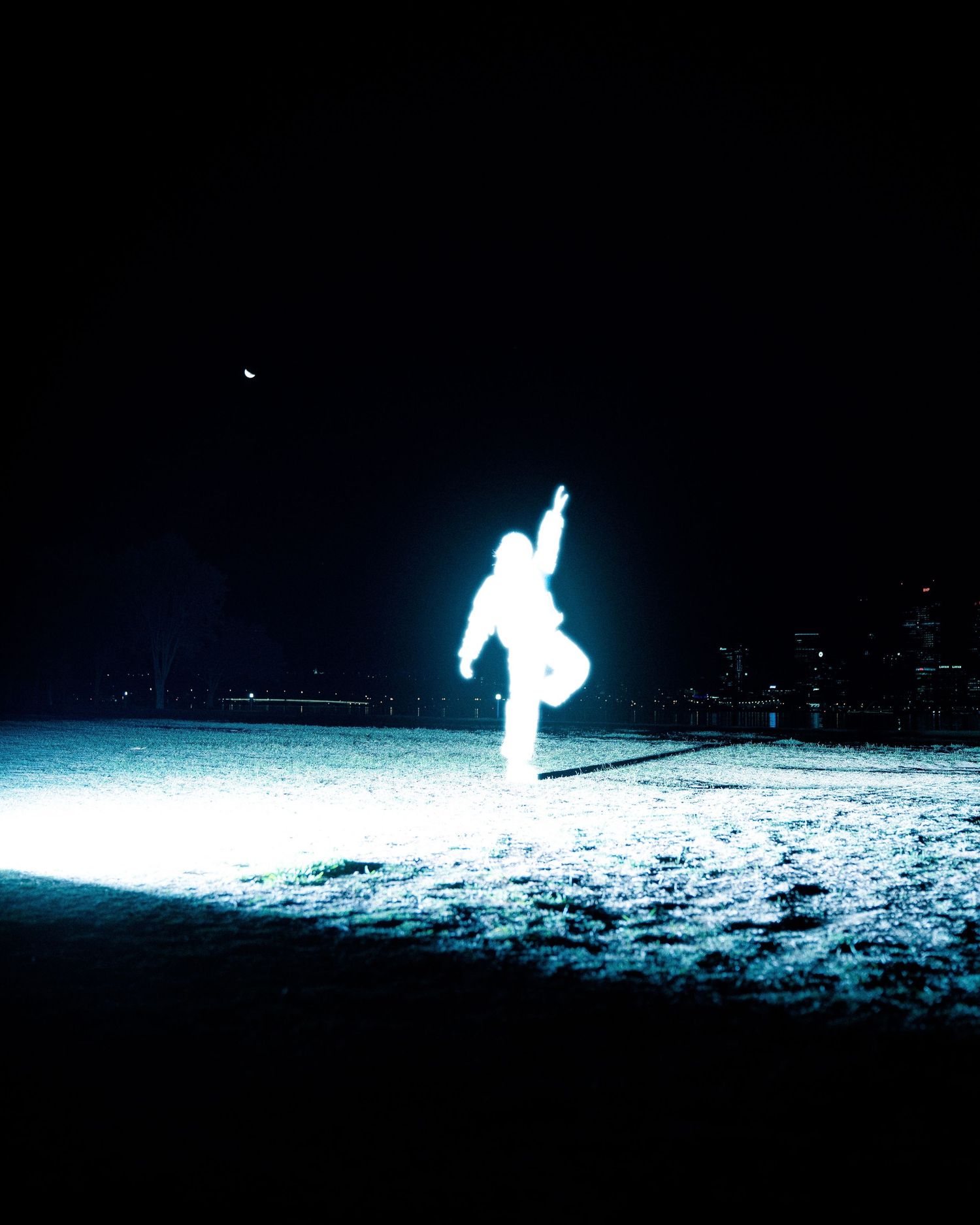 Glowing silhouette figure performs dance moves on snowy ground at night with cityscape in background.