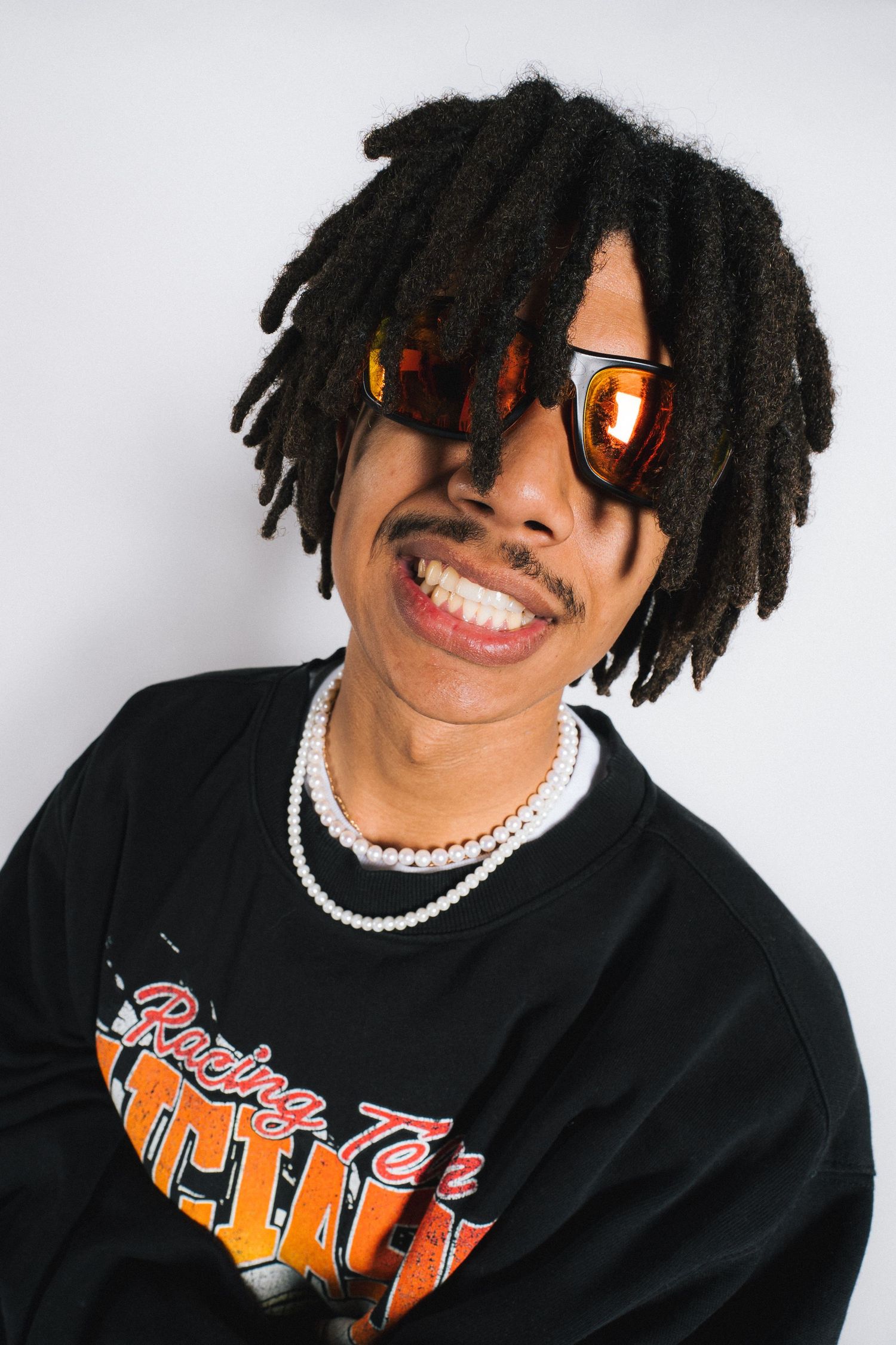 Person in black sweatshirt and sunglasses smiling against white background in creative split-panel composition.
