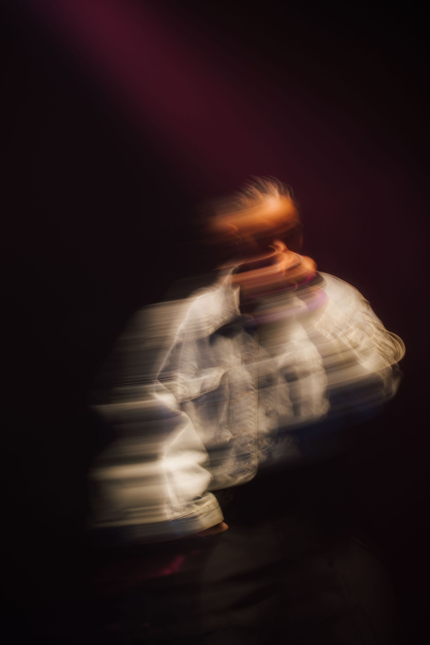 An abstract motion-blurred figure in white clothing spinning against a dark background creates a ghostly effect.
