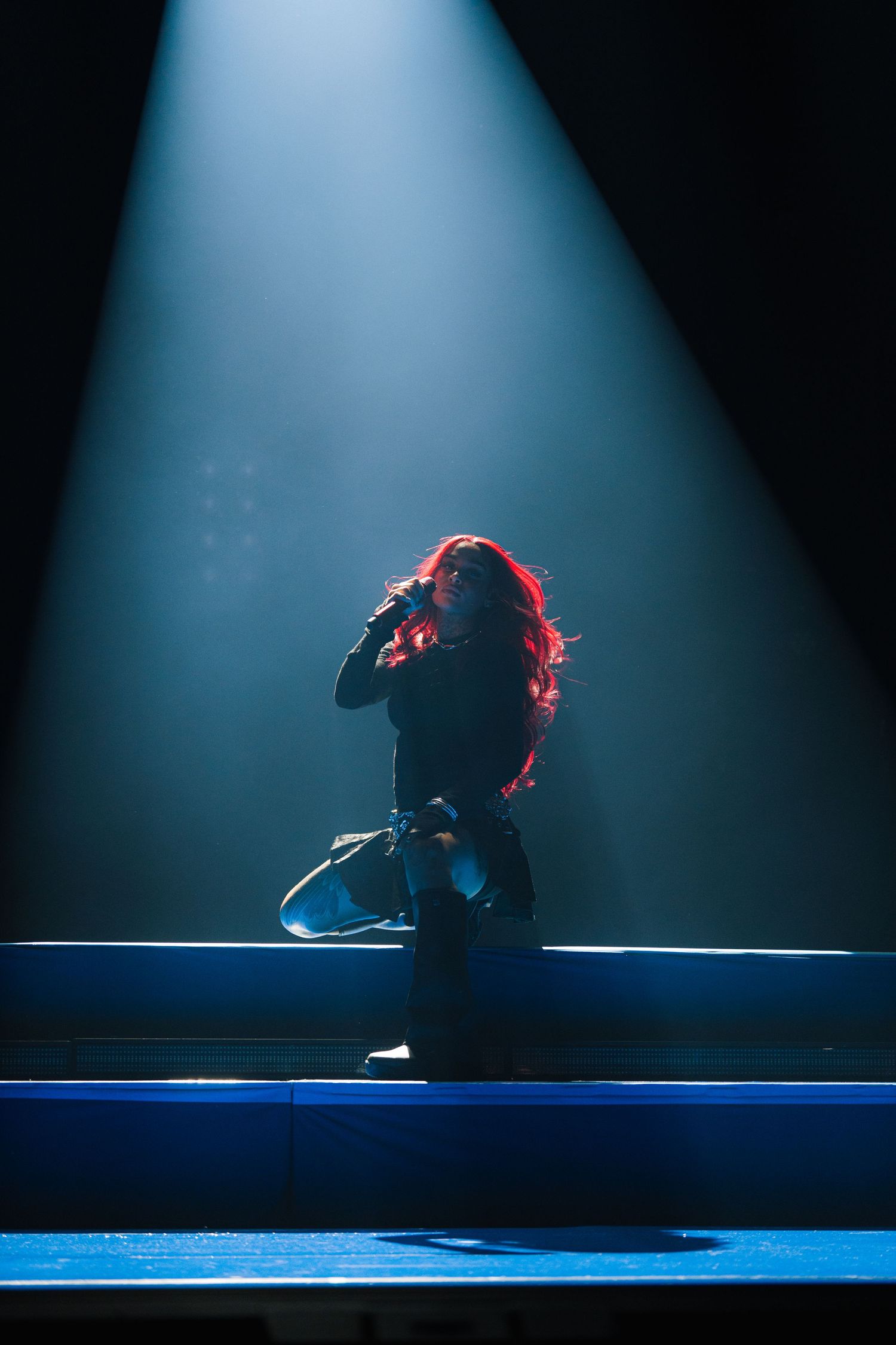 Dramatic silhouette of a performer in a spotlight on stage with illuminated blue steps creating a theatrical atmosphere.