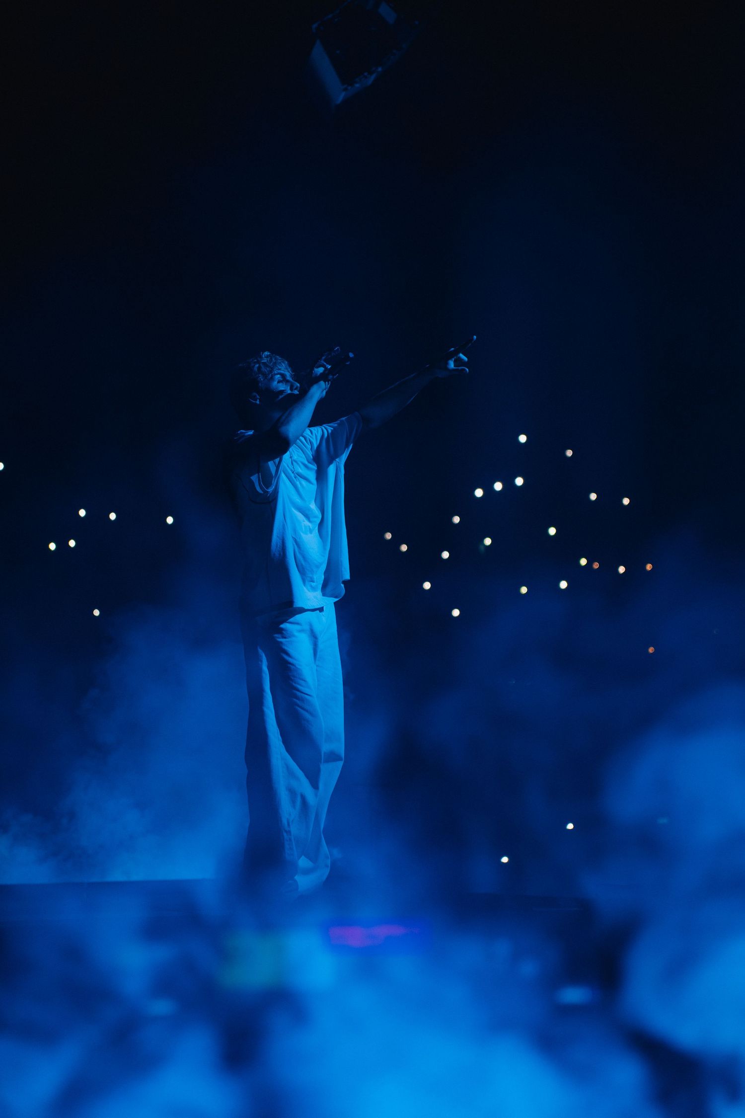 Performer on stage in white outfit silhouetted against deep blue lighting and bokeh lights in background.
