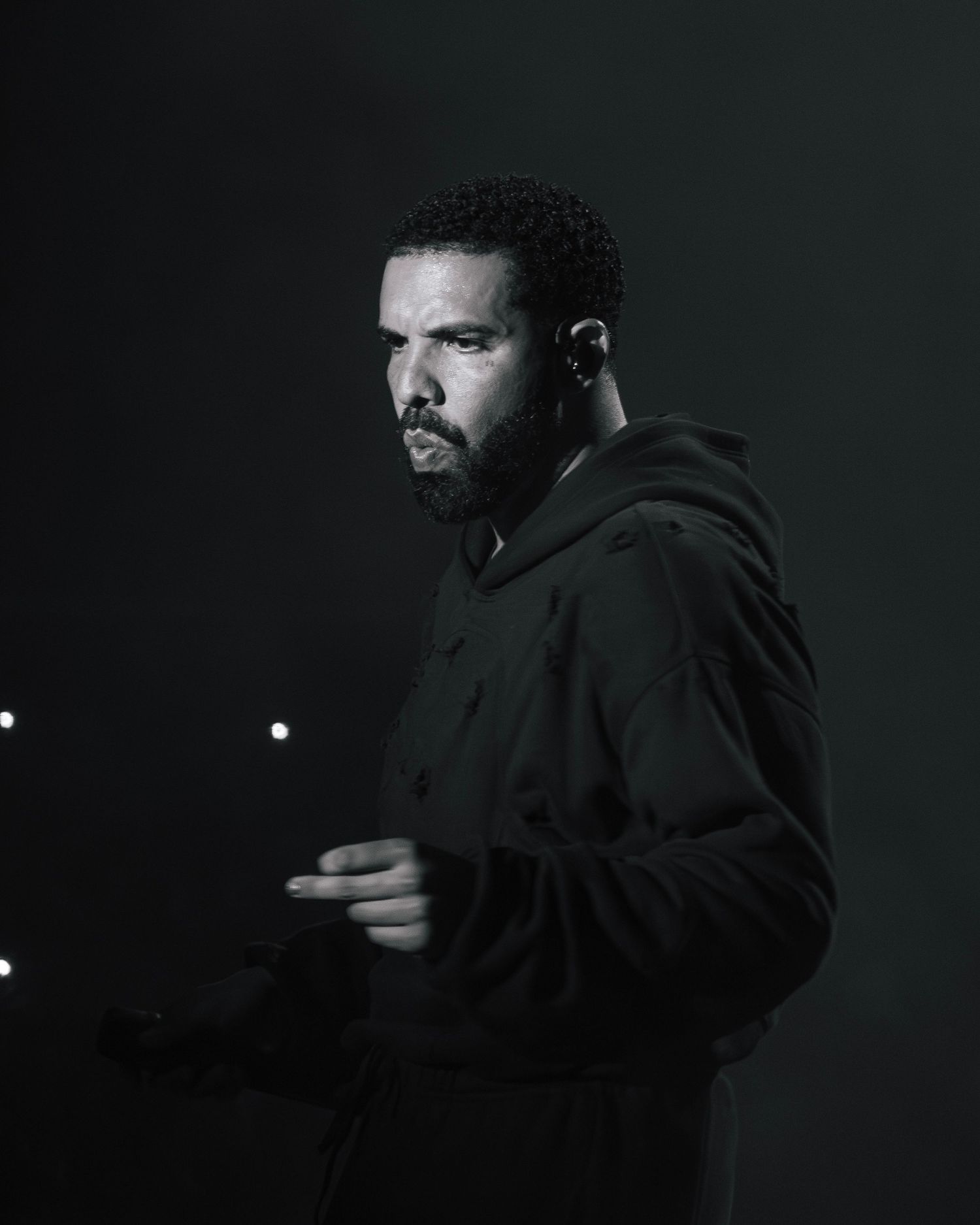 A performer in a black hoodie stands on a dimly lit stage during a dramatic musical performance.