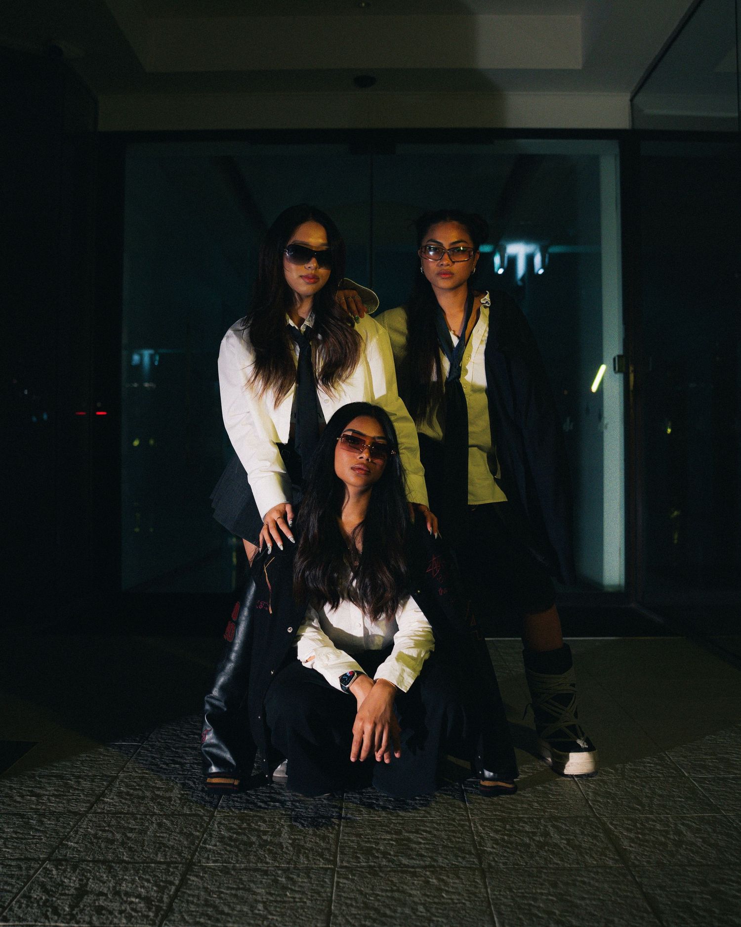 Group photo of three people in white and dark outfits against dim interior backdrop.