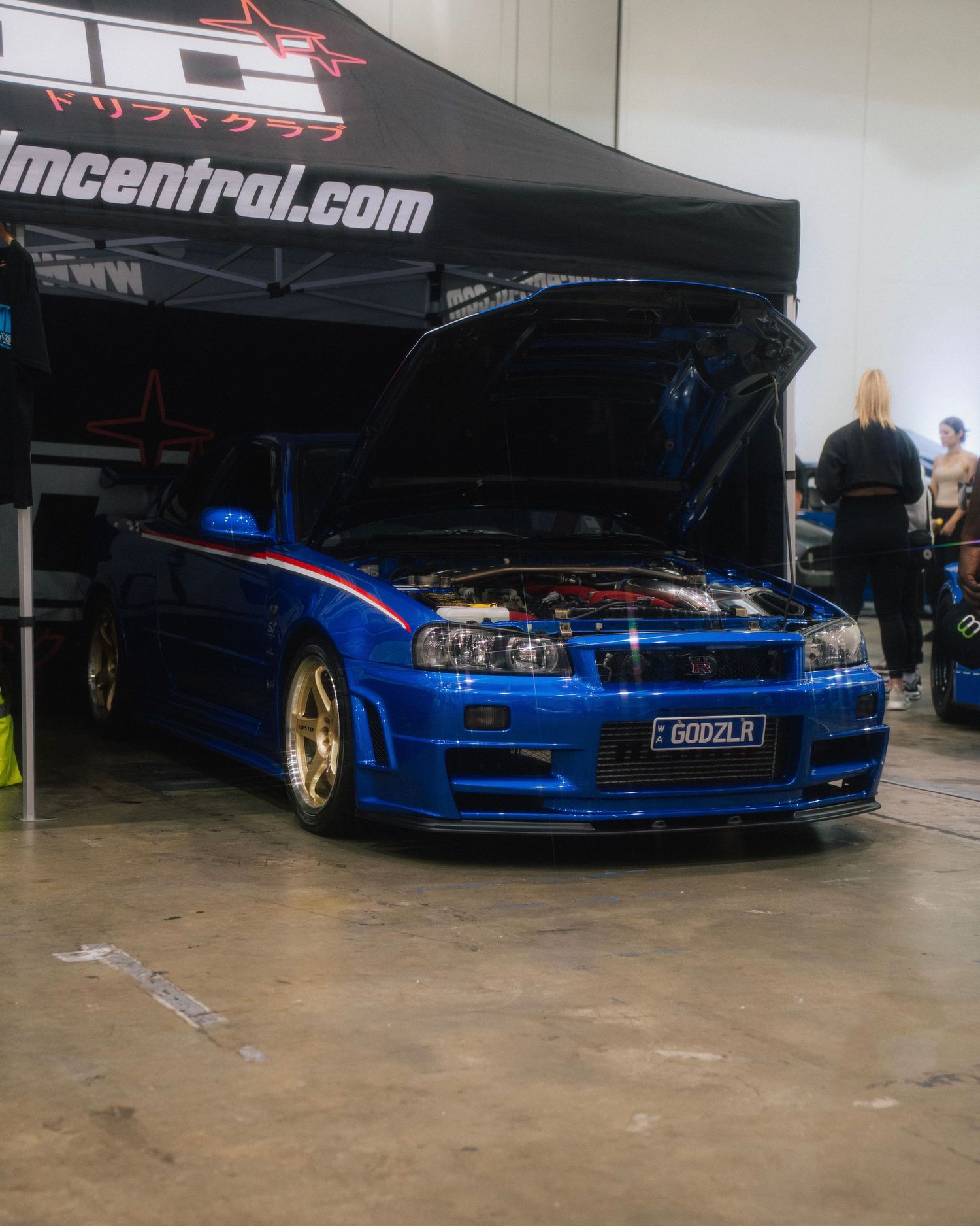 Modified blue Nissan Skyline GT-R with hood open on display at indoor car show.