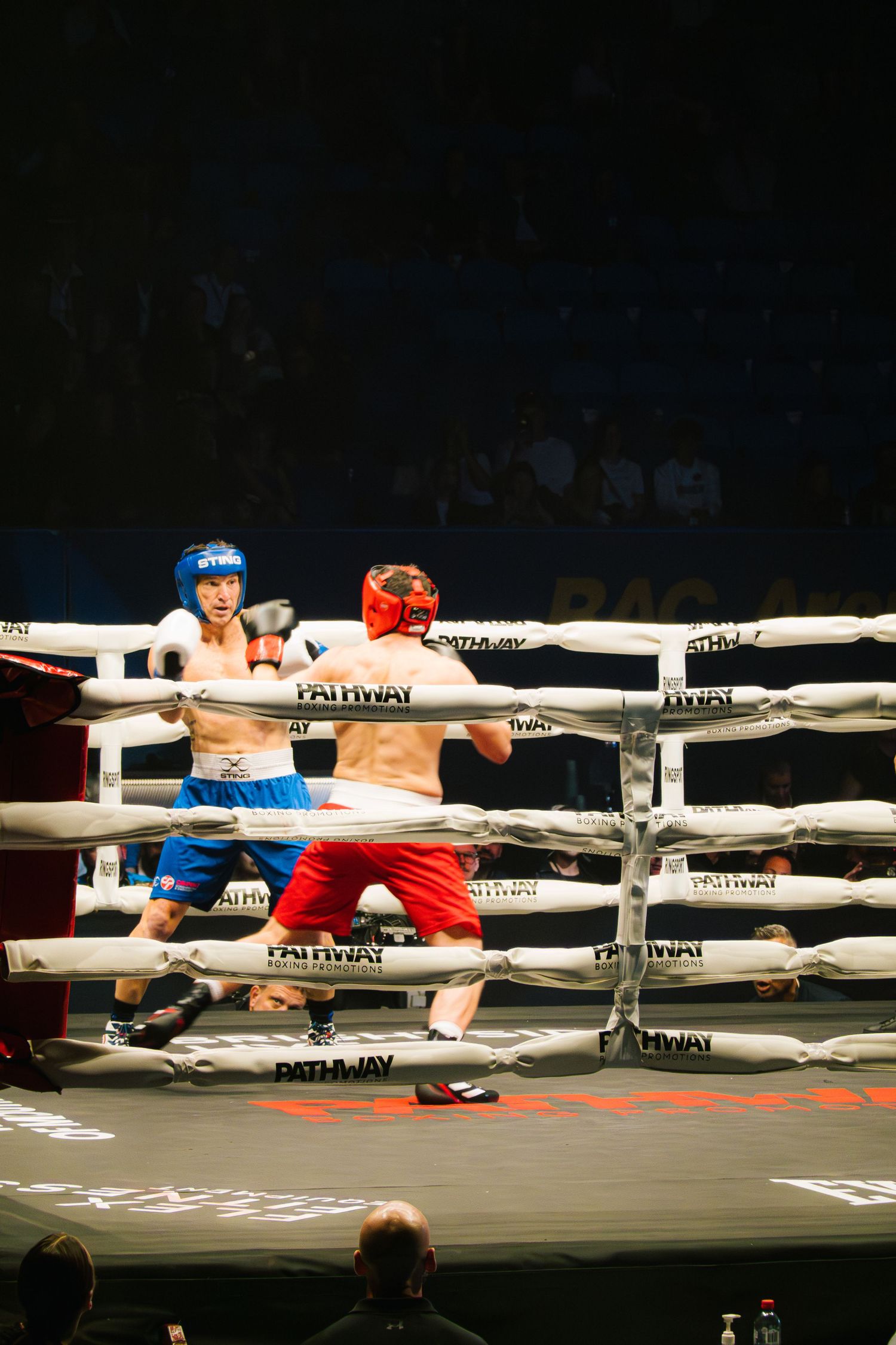 Two boxers in red and blue gear exchange punches during competitive match.