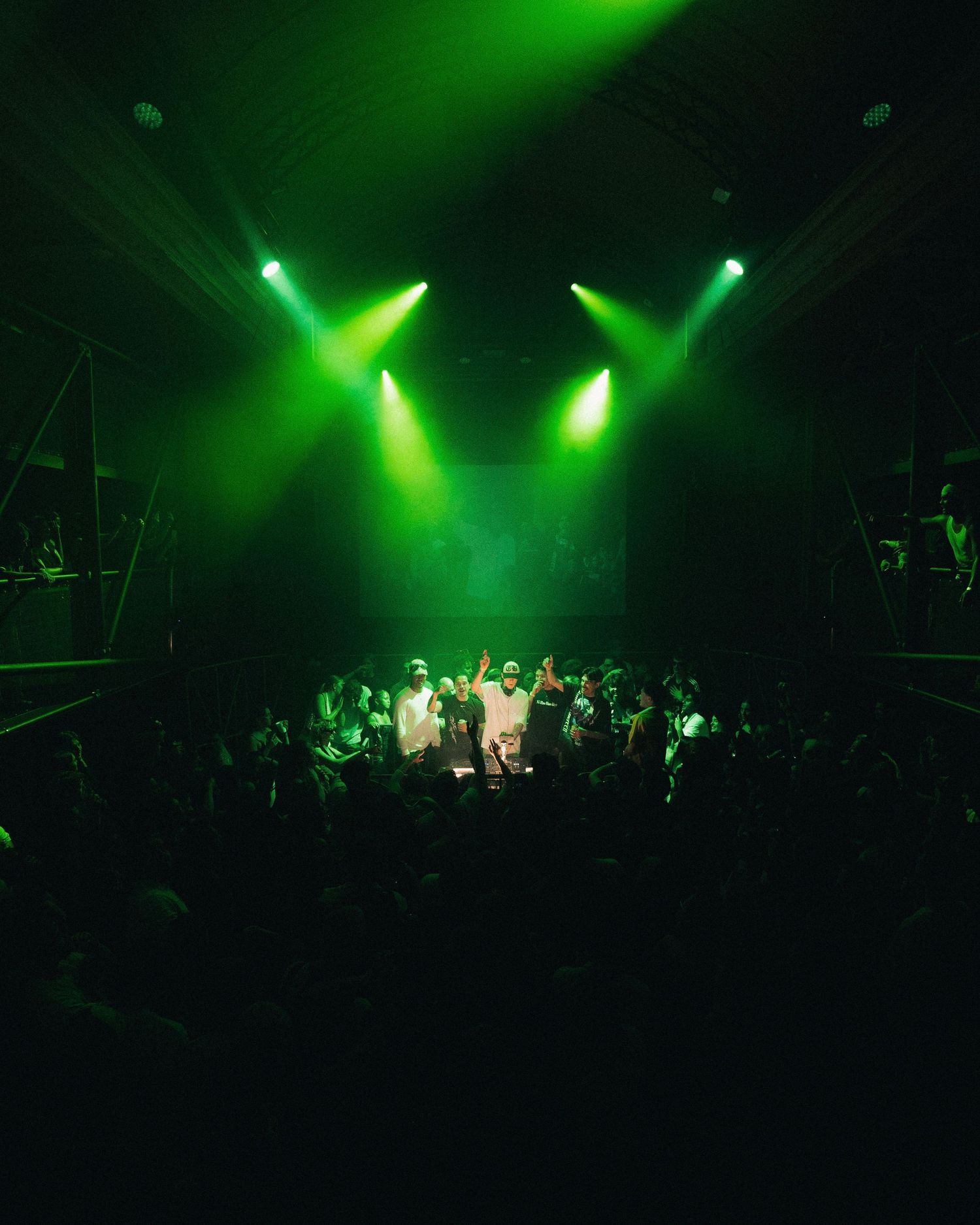 Music performance in a dark venue with vibrant green stage lighting illuminating performers and audience.