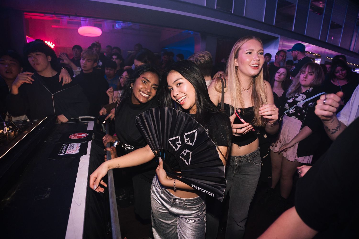 Nightclub crowd dancing and enjoying music with colorful purple lighting at a party venue.
