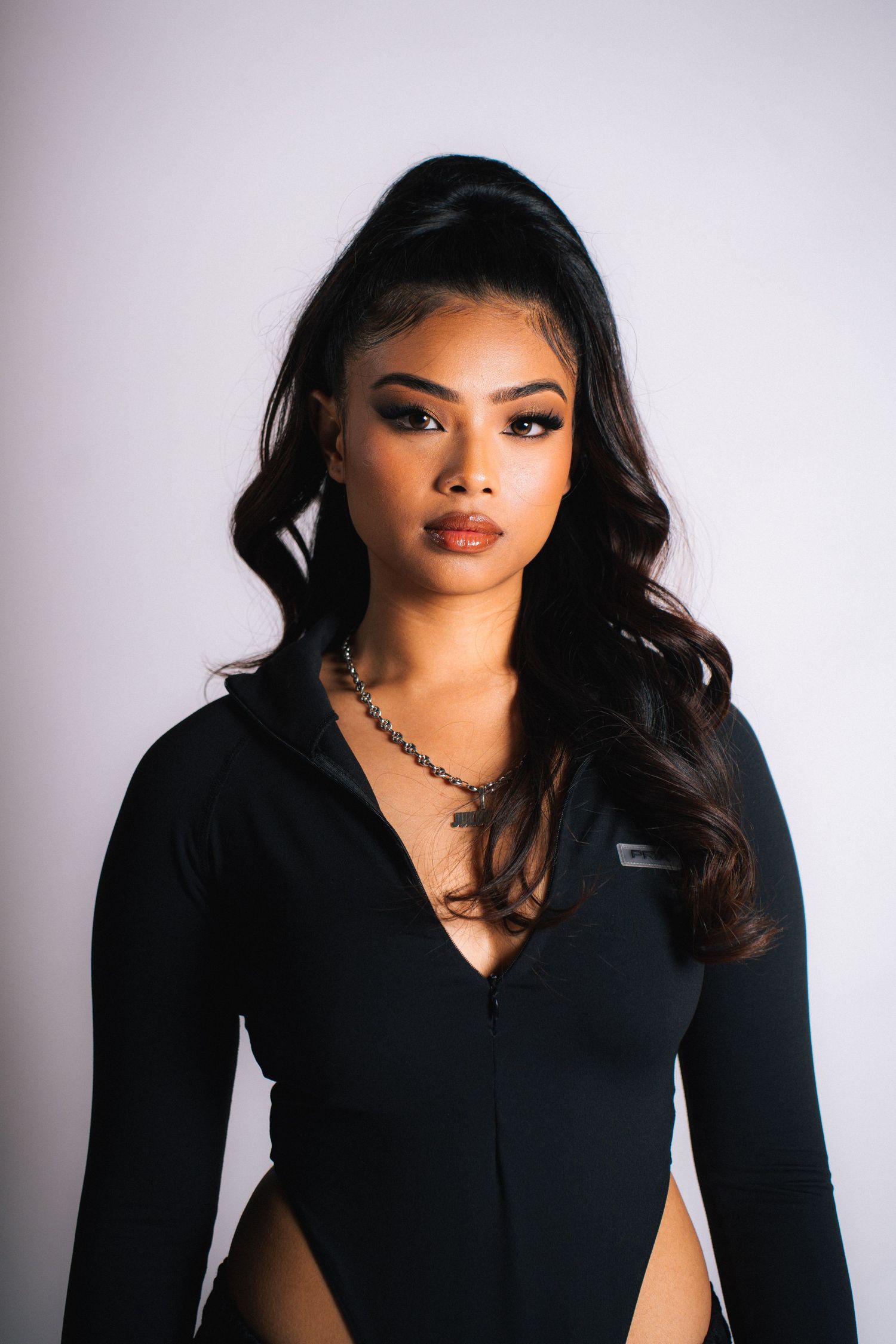 Fashion portrait showing figure in black v-neck top against light background with dramatic lighting.