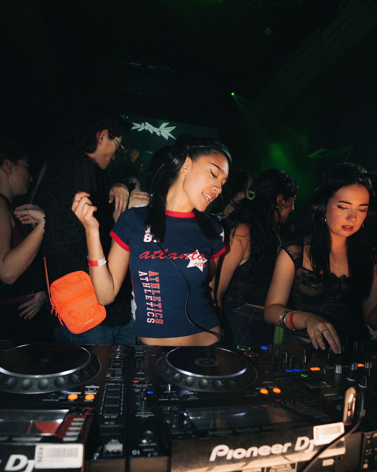 DJ performing at a nightclub using Pioneer DJ equipment in dark atmospheric lighting.