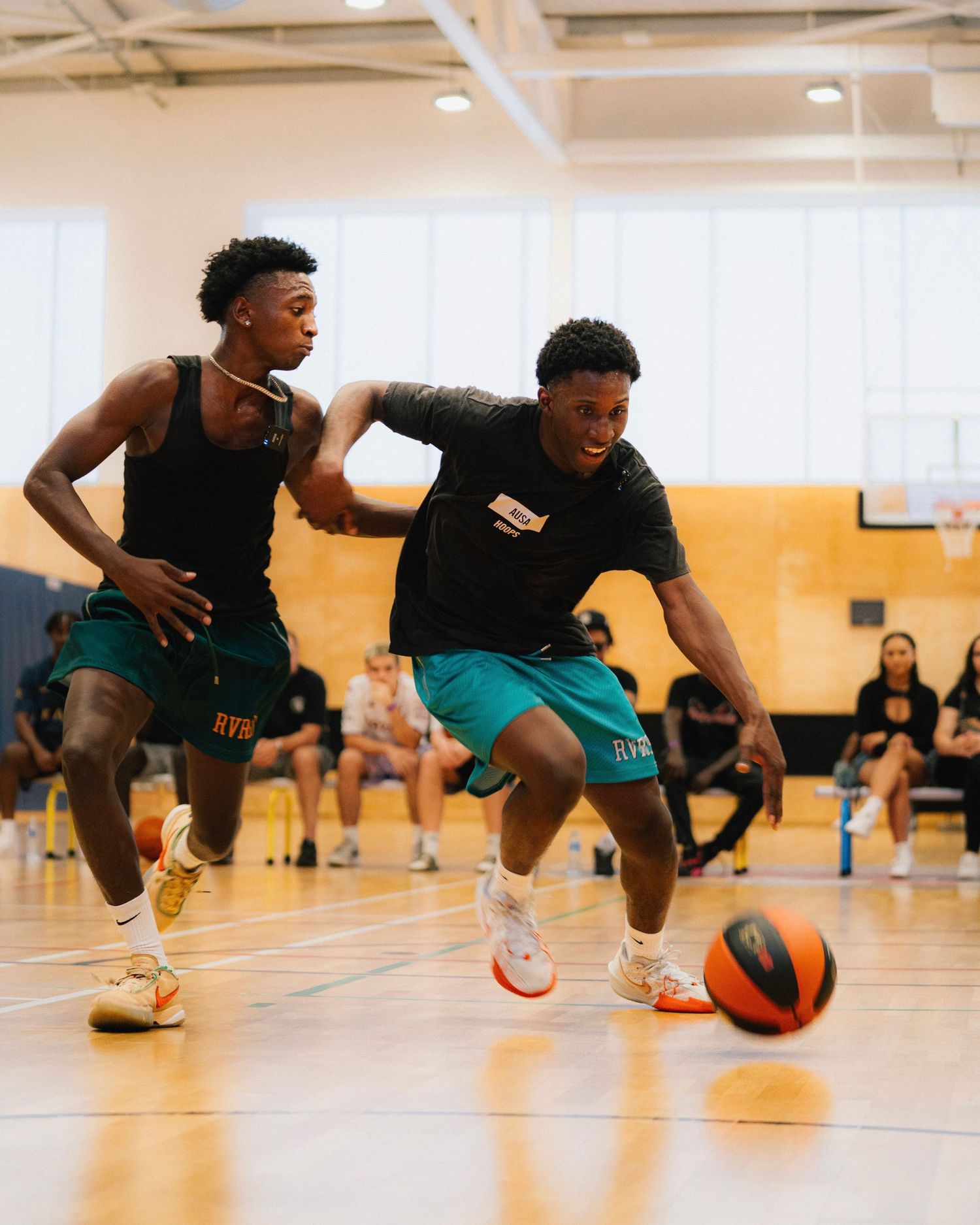 Basketball players in black and teal uniforms competing for the ball during an indoor game.