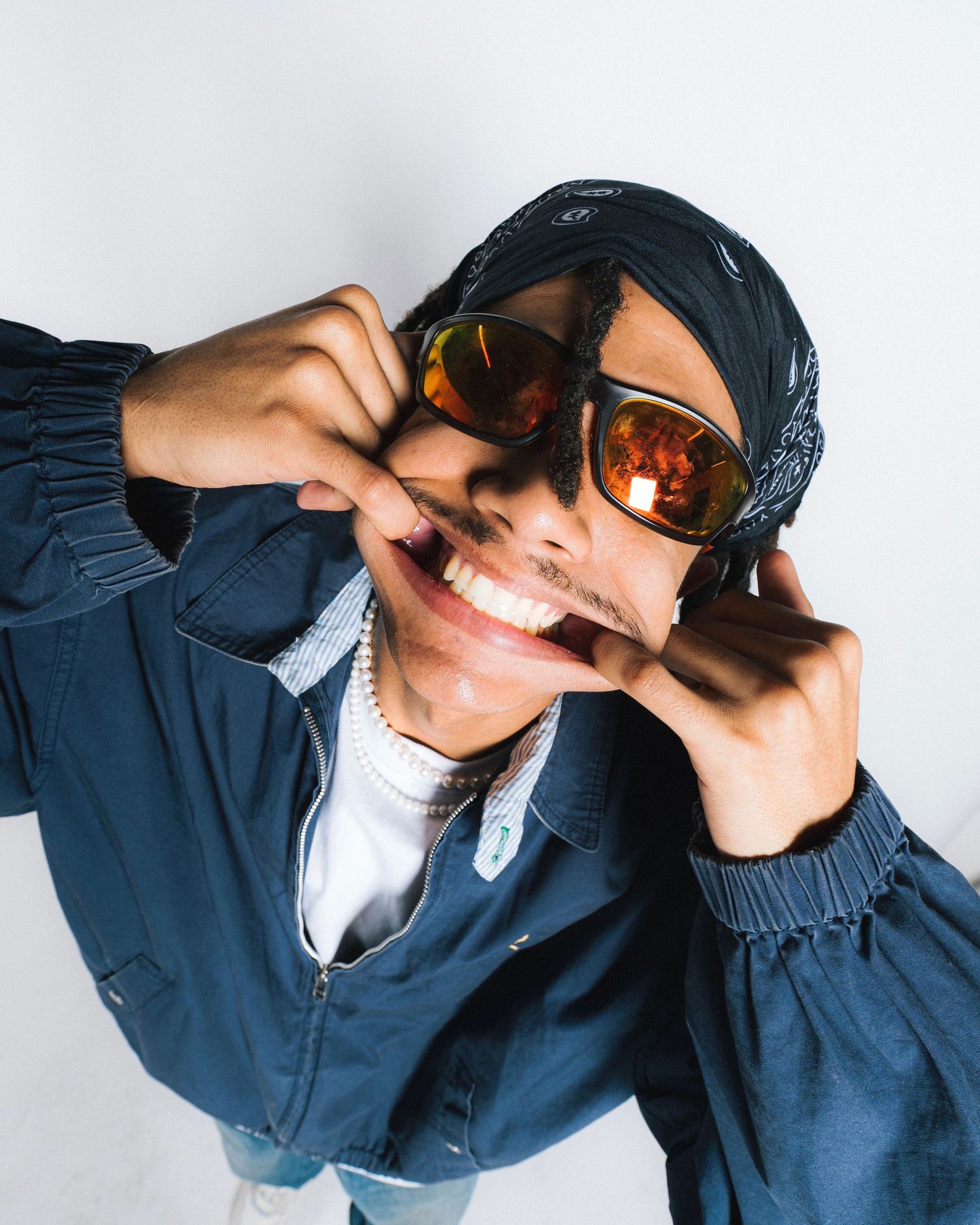 Person in navy blue jacket and orange-tinted sunglasses making playful expression against white background.