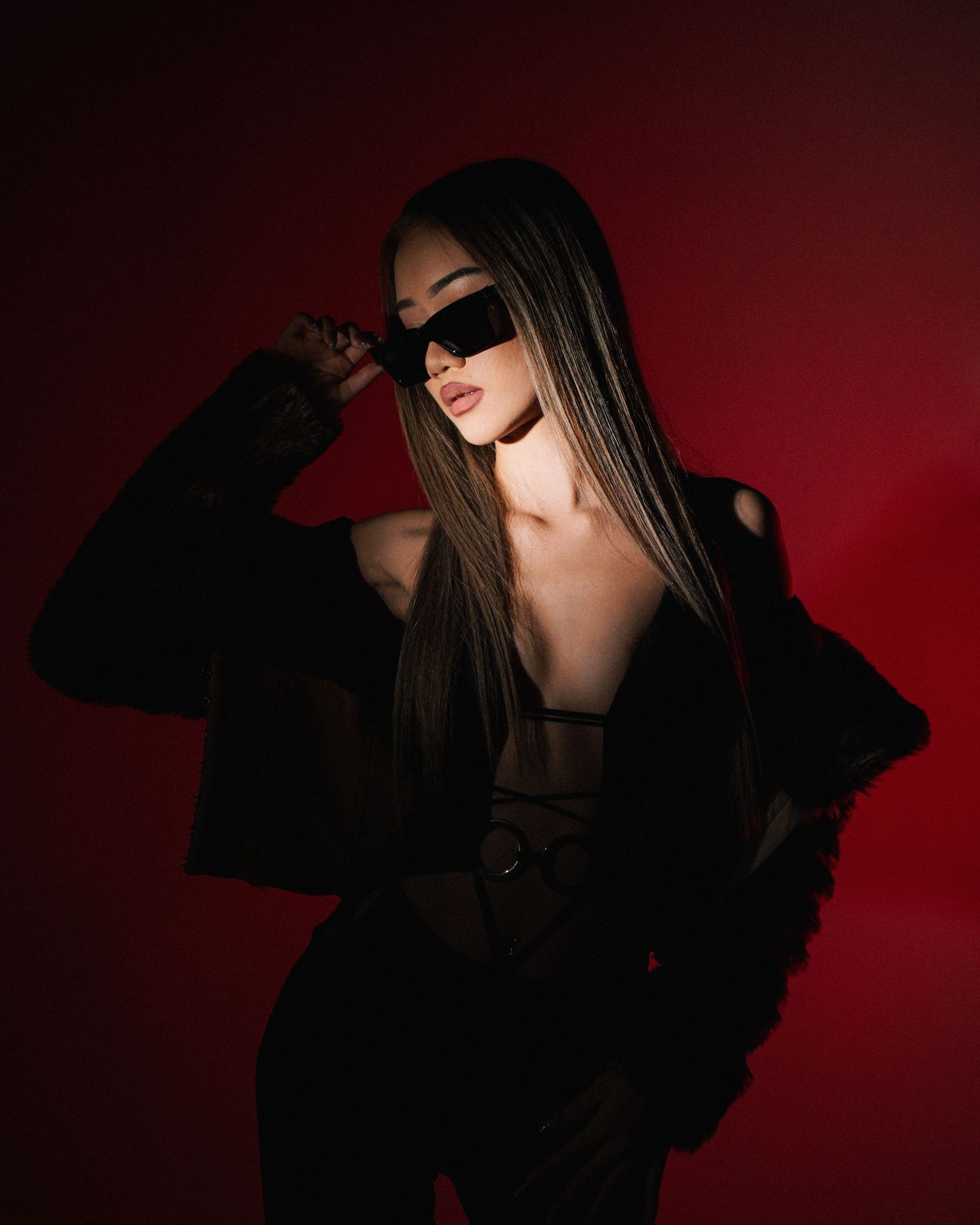 Dramatic fashion portrait with model in black outfit against dark red background.