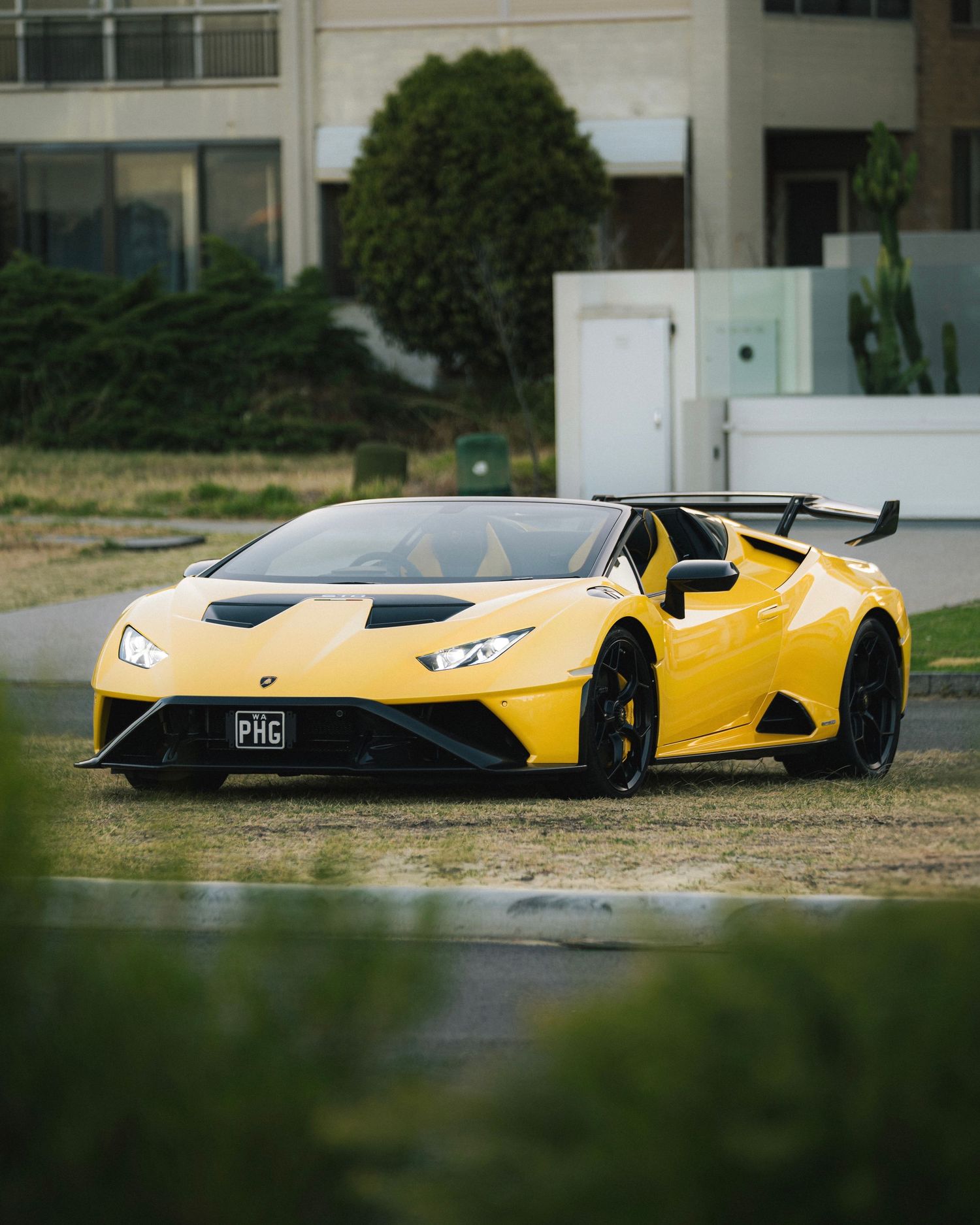 Yellow Lamborghini supercar parked on grass with modern building in background.