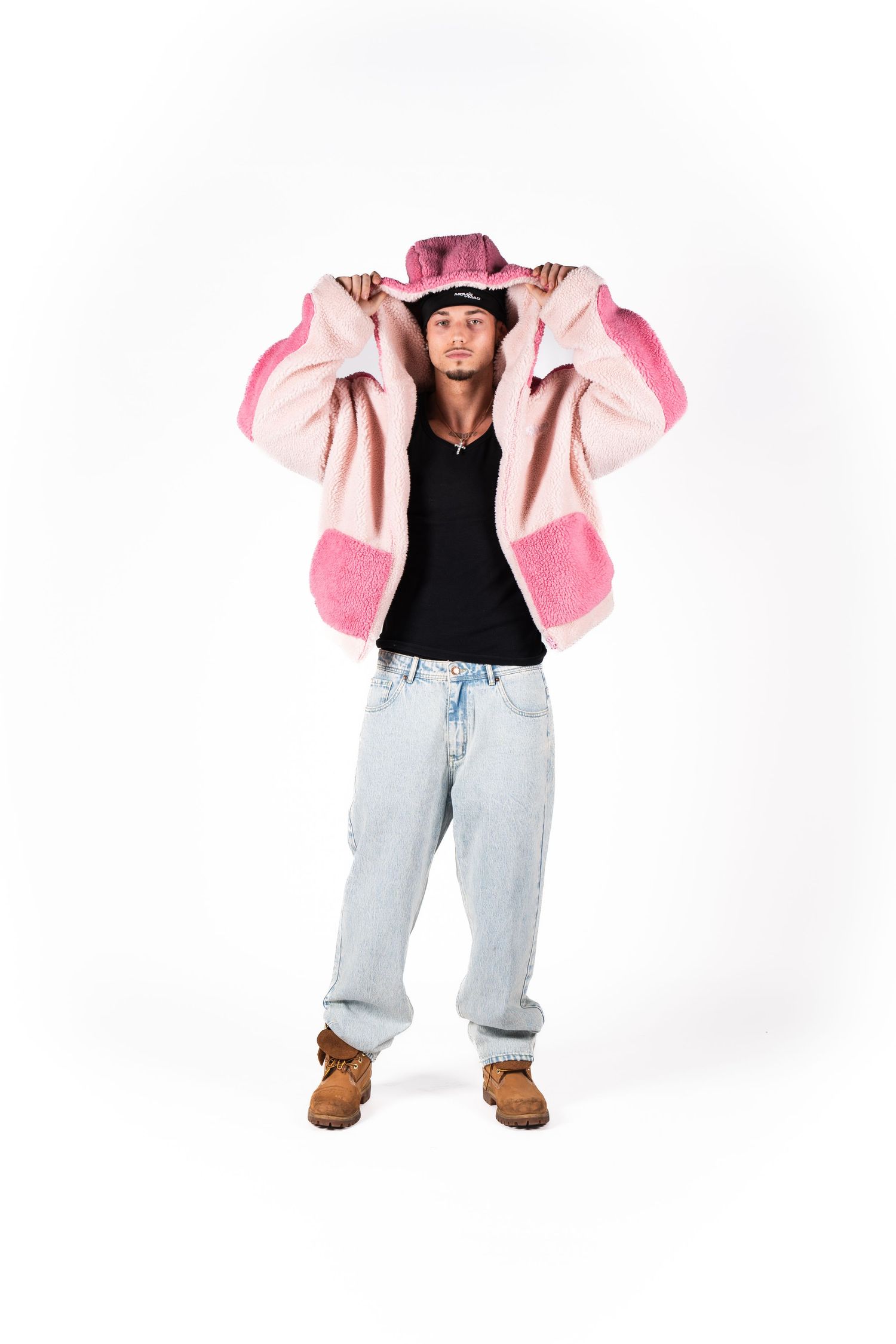 Model wearing pink and beige color block jacket with black top and light wash baggy jeans against white background.