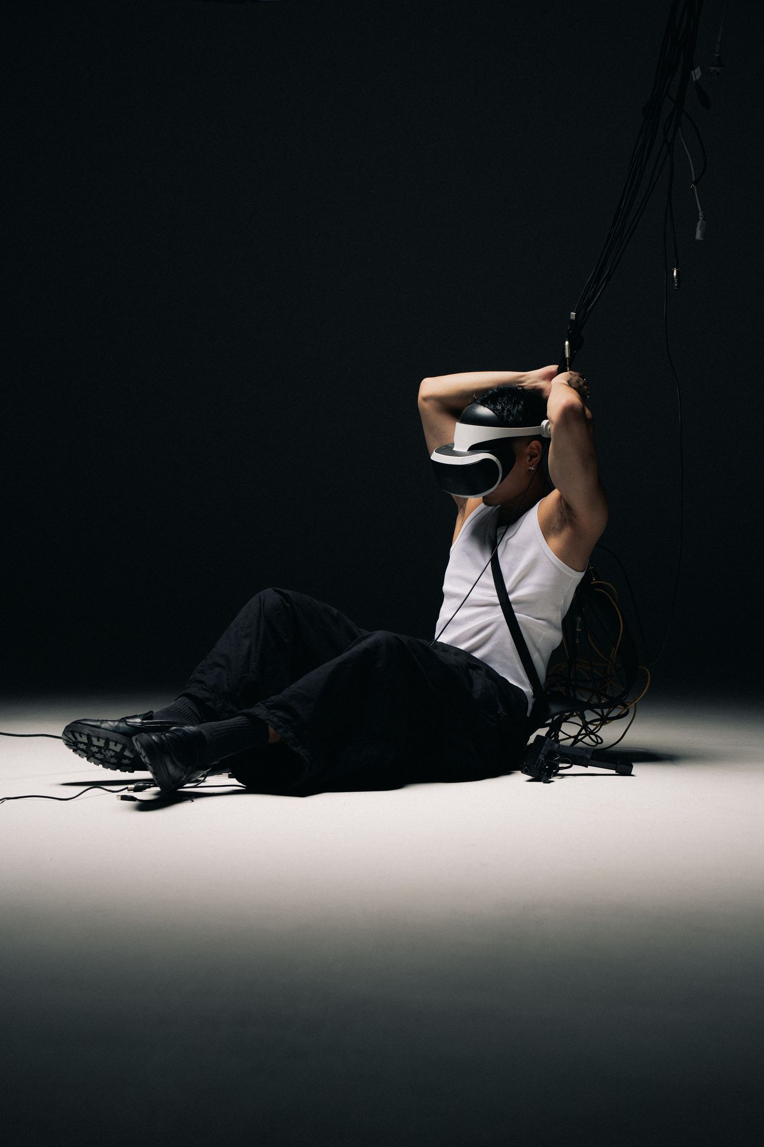 Person wearing VR headset sits on floor against dark background while immersed in virtual reality experience.