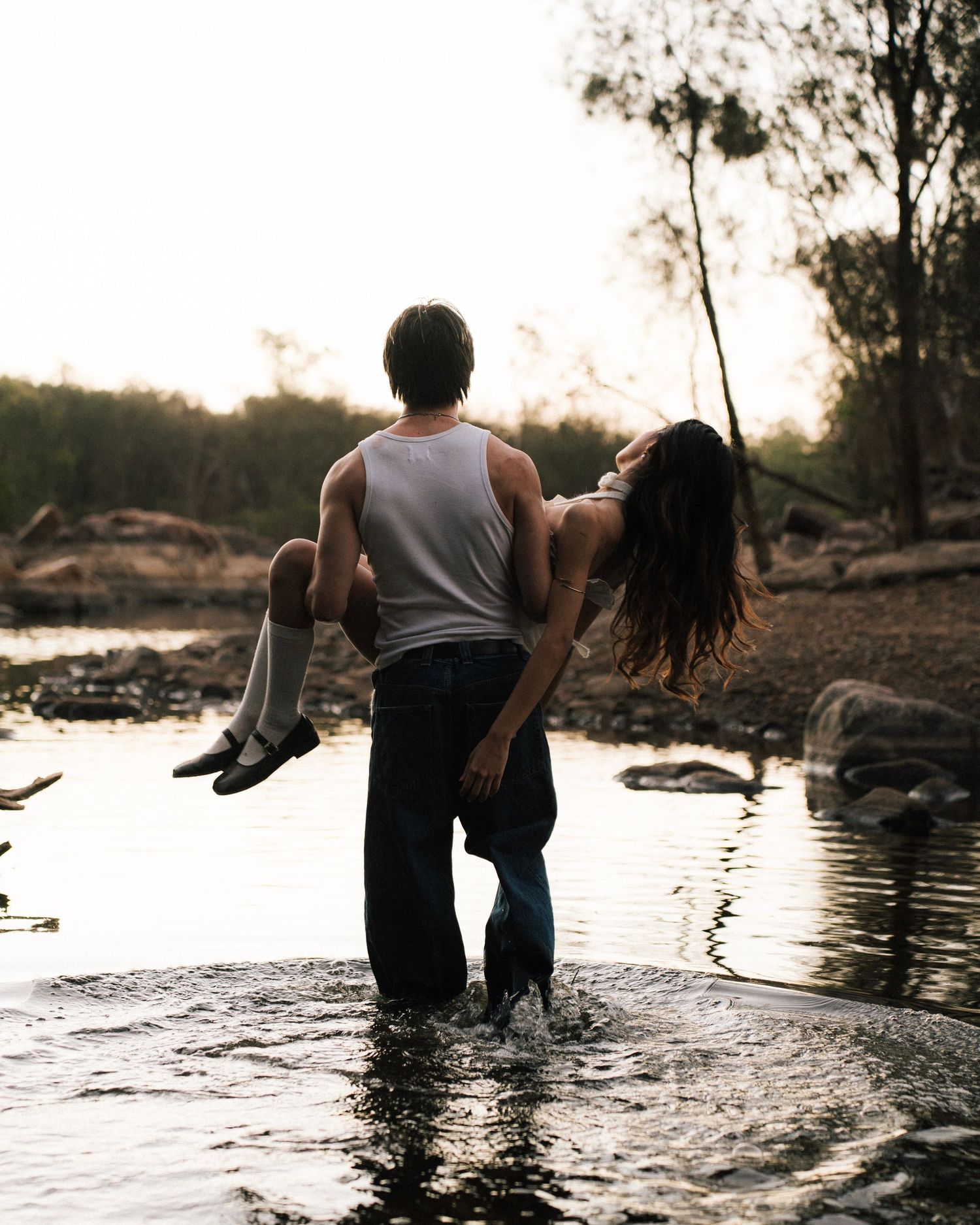Two people stand in shallow water at sunset, creating a romantic silhouette against the golden light.