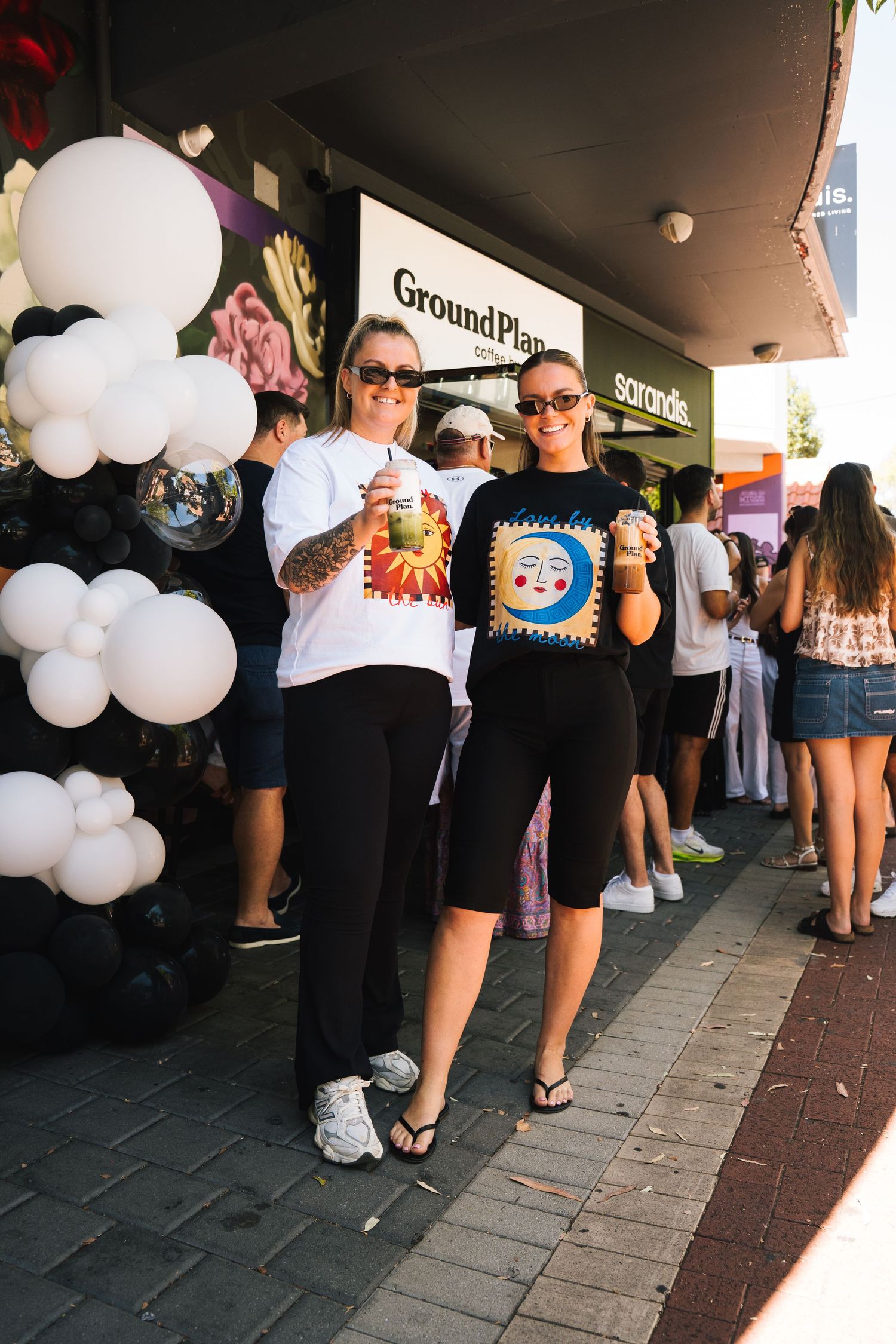 A series of people waiting in line outside a store with white balloons decorating the entrance.