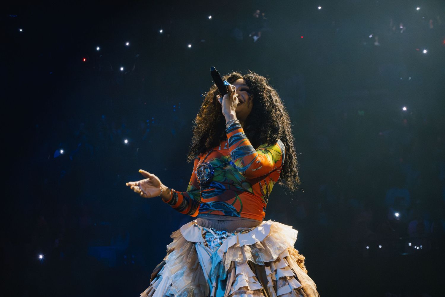 Dancer in colorful dress performing on dark stage with starry background and dramatic lighting effect.