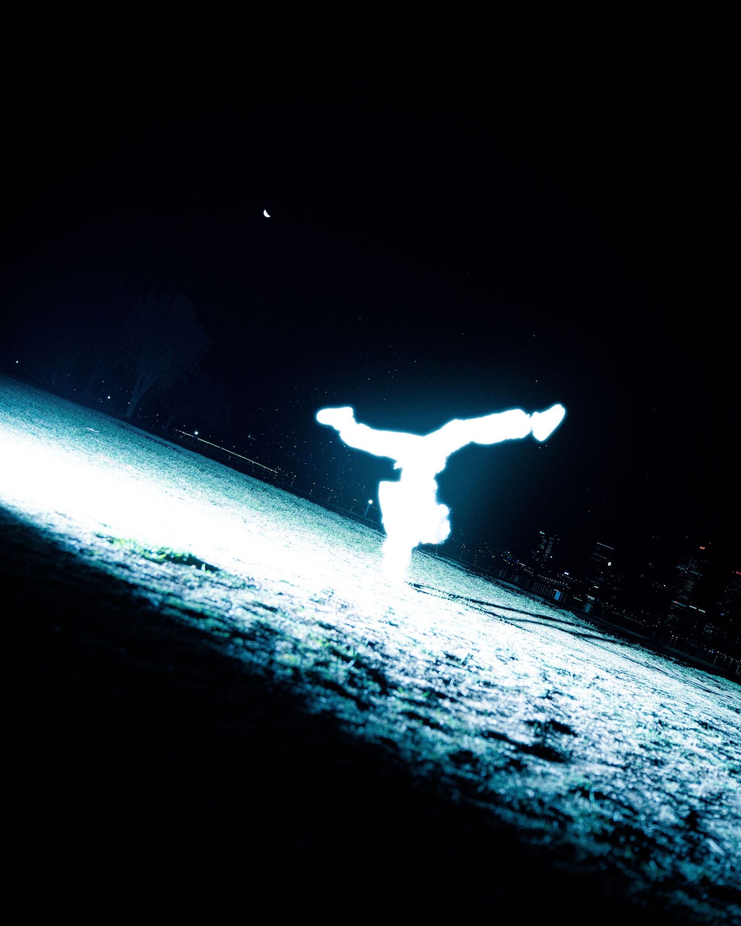 Silhouette of person doing handstand captured in blue light against dark background.