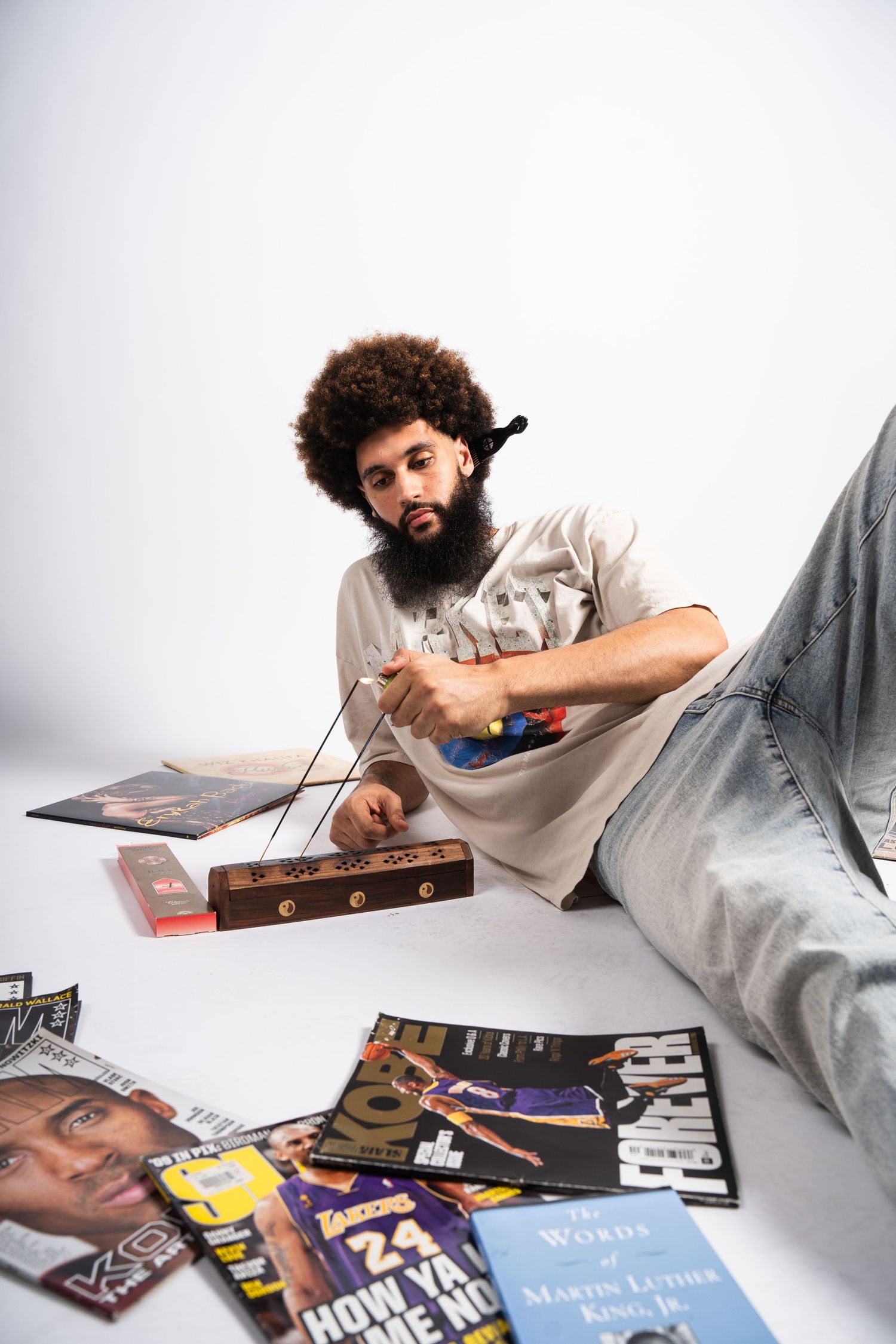 A person with curly afro hair lying down reading through vinyl records and books in a casual setting.